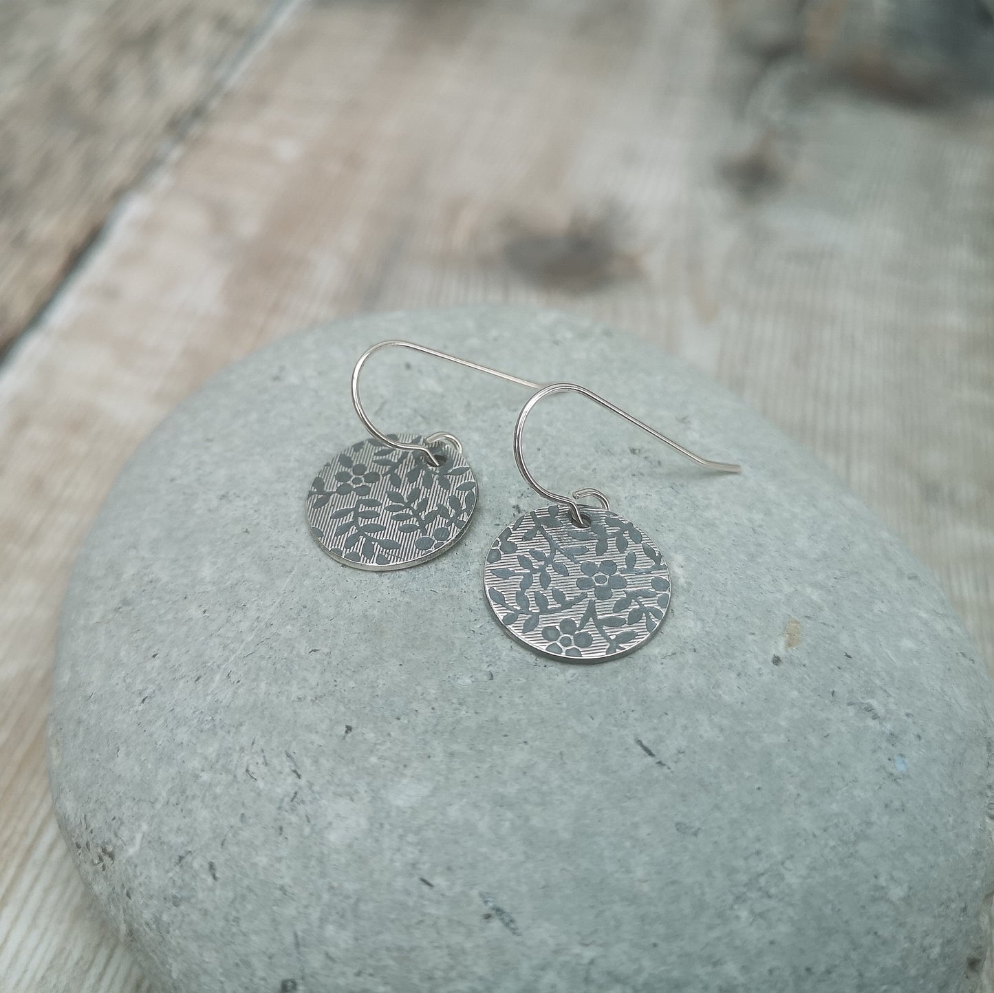 Each earring is a Sterling Silver disc stamped with a floral pattern of flowers with 5 petals and leaves suspended from silver earring wire.