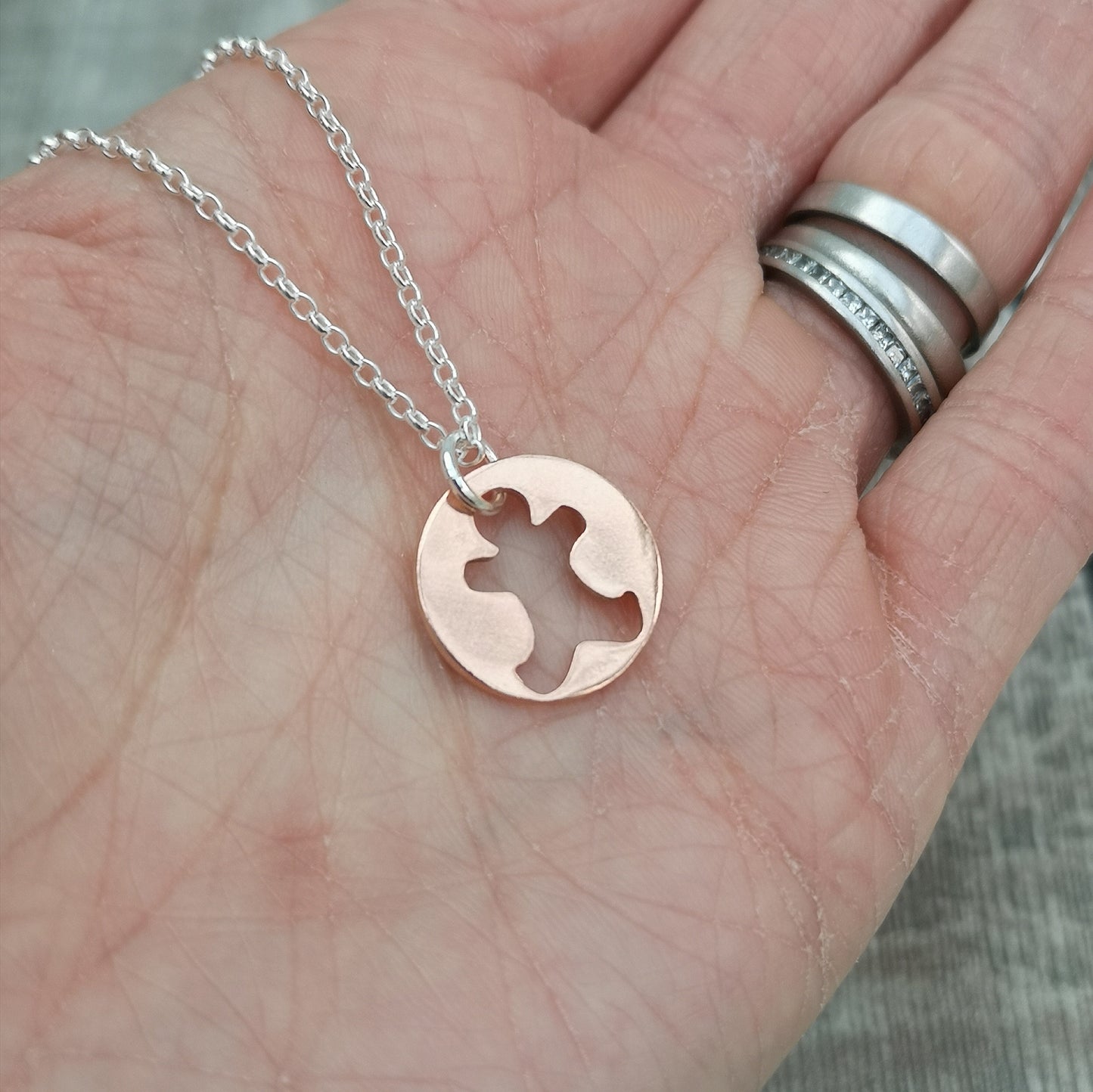 Round disc shaped copper pendant, approximately 15mm diameter. Traditional gingerbread man shape cut out from middle of circle. Attached to silver chain with small, round silver link through gingerbread man cut out.
