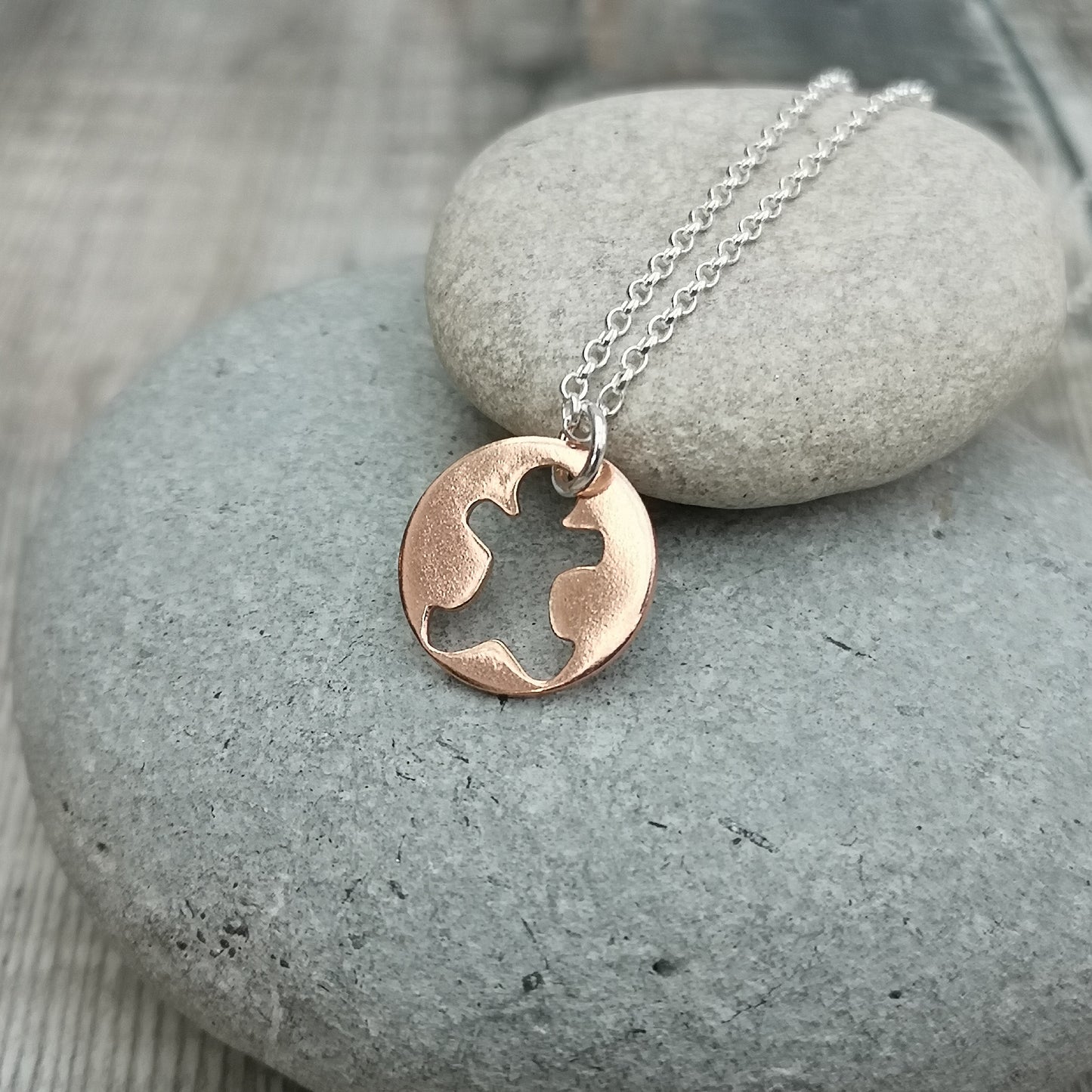 Round disc shaped copper pendant, approximately 15mm diameter. Traditional gingerbread man shape cut out from middle of circle. Attached to silver chain with small, round silver link through gingerbread man cut out.