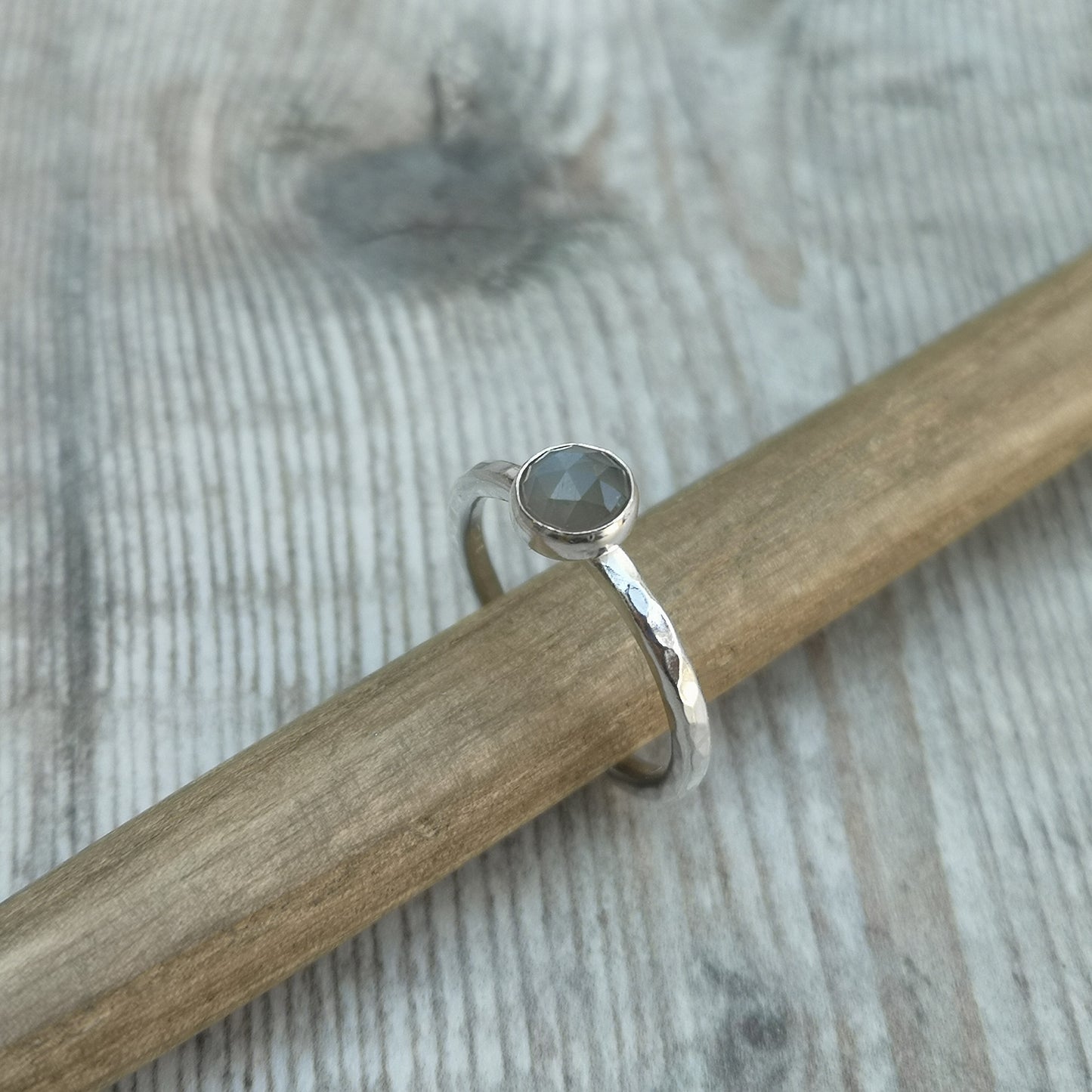 Pale grey coloured moonstone gemstone with diamond cut texture, set in simple silver bezel mounted on top of Sterling Silver band approx. 2mm wide with hammered texture finish.