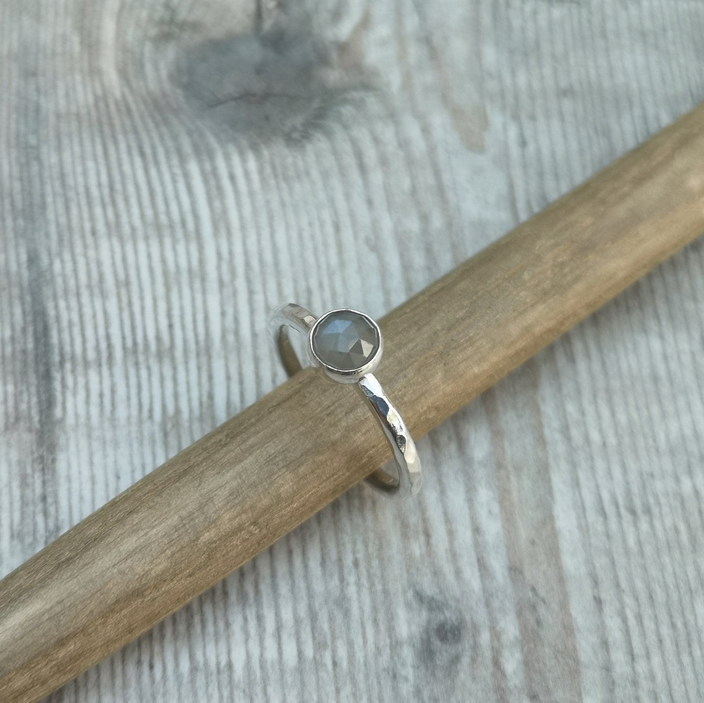 Pale grey coloured moonstone gemstone with diamond cut texture, set in simple silver bezel mounted on top of Sterling Silver band approx. 2mm wide with hammered texture finish.