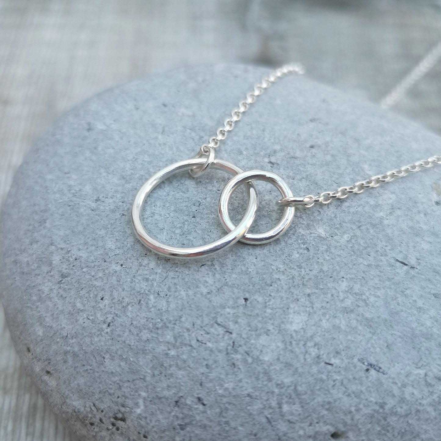A large smooth silver open circle is linked to a smaller open circle, each is attached to one end of a silver chain.