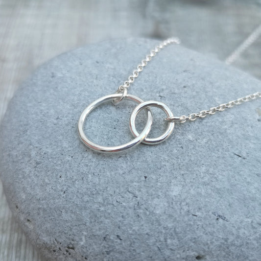 A large smooth silver open circle is linked to a smaller open circle, each is attached to one end of a silver chain.