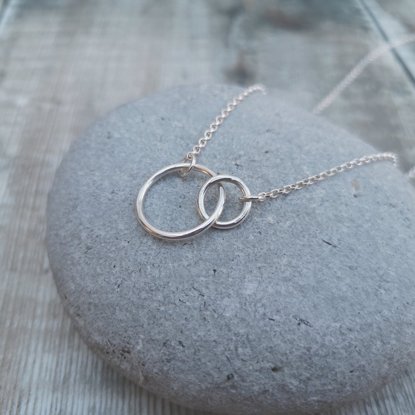 A large smooth silver open circle is linked to a smaller open circle, each is attached to one end of a silver chain.