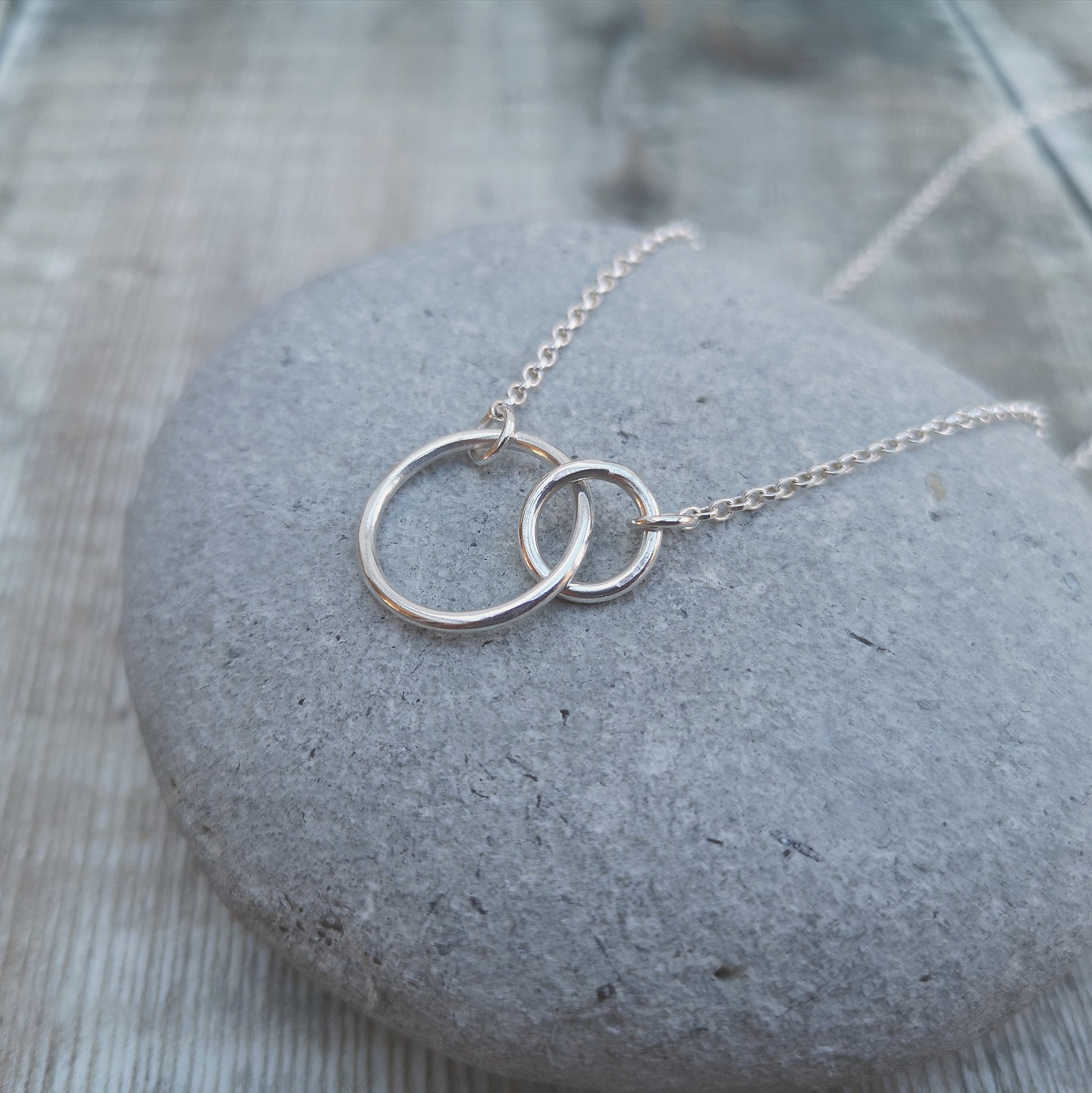 A large smooth silver open circle is linked to a smaller open circle, each is attached to one end of a silver chain.