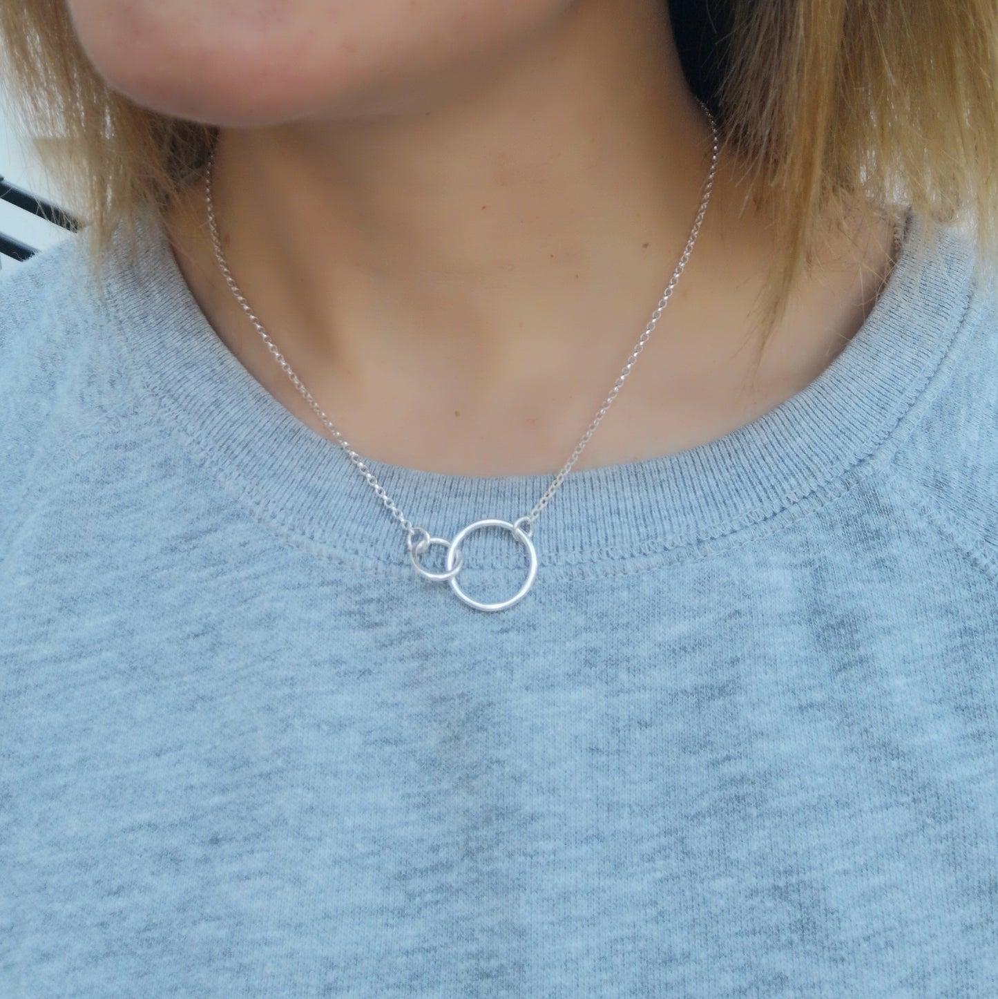 A large smooth silver open circle is linked to a smaller open circle, each is attached to one end of a silver chain.