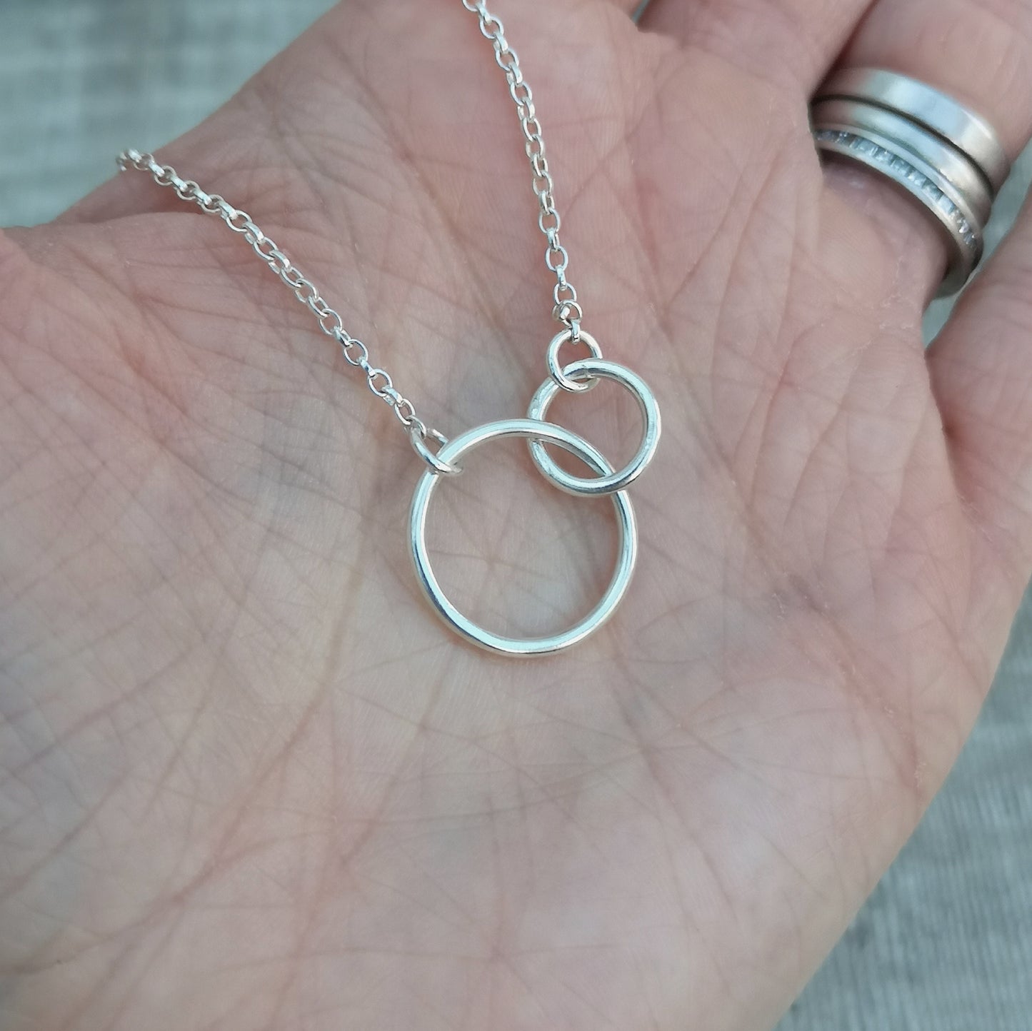 A large smooth silver open circle is linked to a smaller open circle, each is attached to one end of a silver chain.
