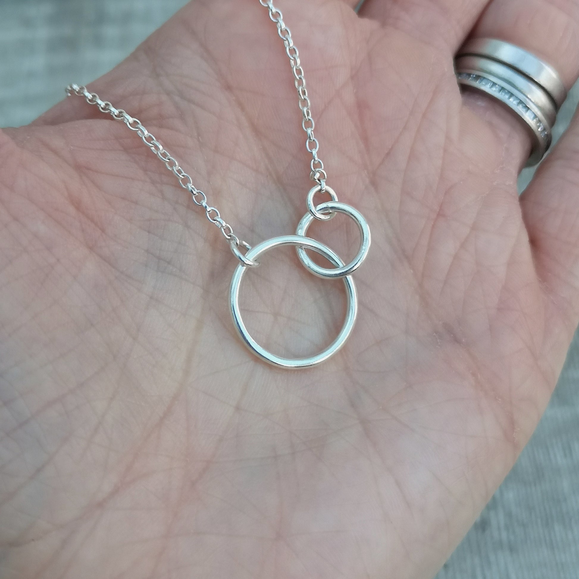 A large smooth silver open circle is linked to a smaller open circle, each is attached to one end of a silver chain.