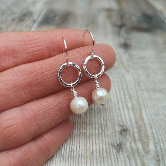Each earring is a small Sterling Silver open circle with hammered texture suspended from silver earring wire. Suspended from the circle is a sphere shaped pearl.