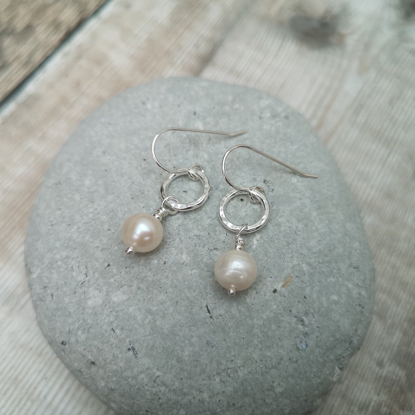 Each earring is a small Sterling Silver open circle with hammered texture suspended from silver earring wire. Suspended from the circle is a sphere shaped pearl.