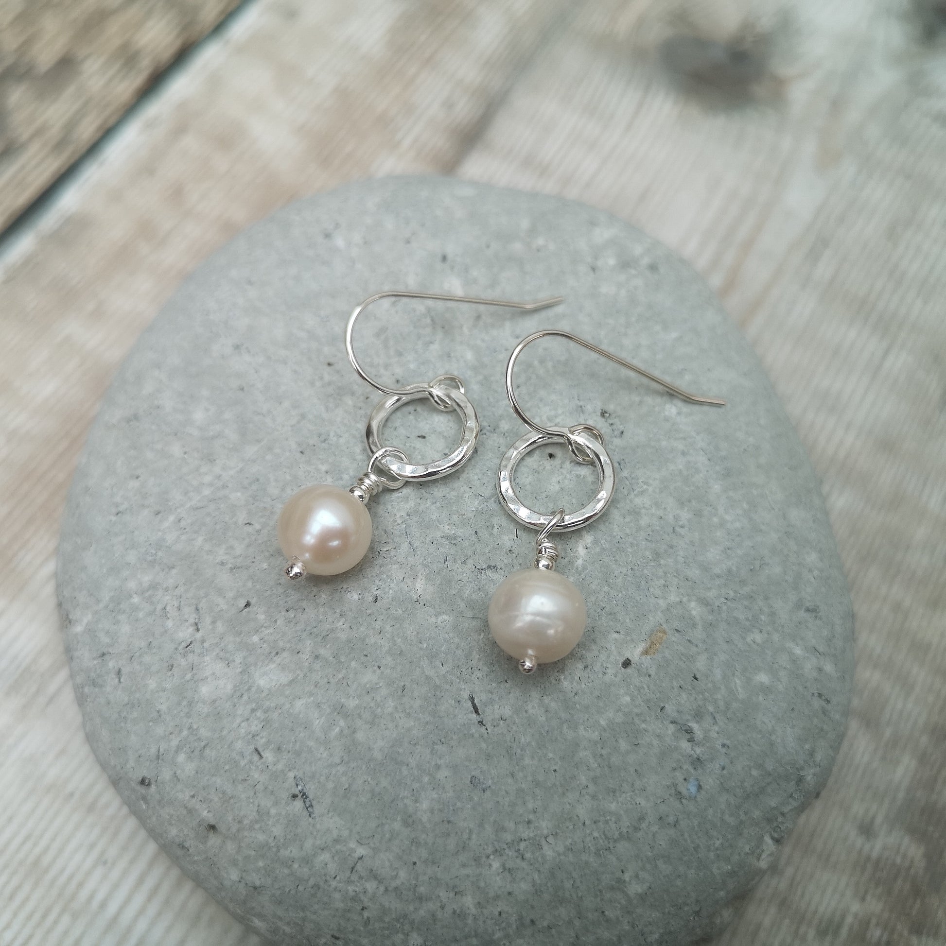 Each earring is a small Sterling Silver open circle with hammered texture suspended from silver earring wire. Suspended from the circle is a sphere shaped pearl.