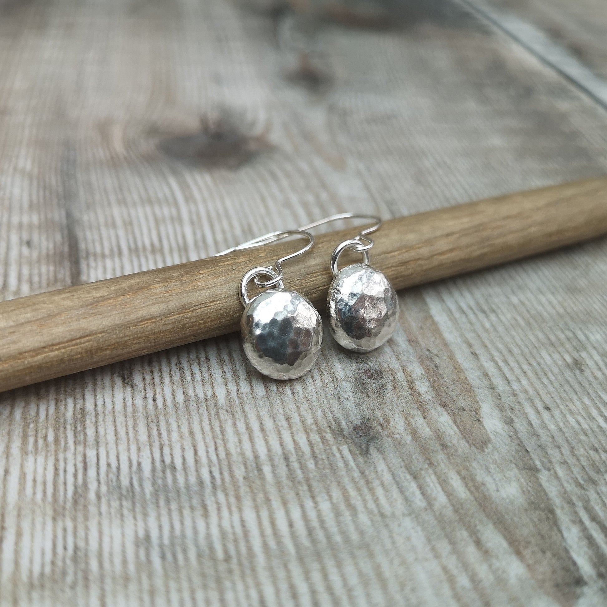 Each earring is a silver round pebble shape pendant with hammered texture finish suspended from a silver earring wire.
