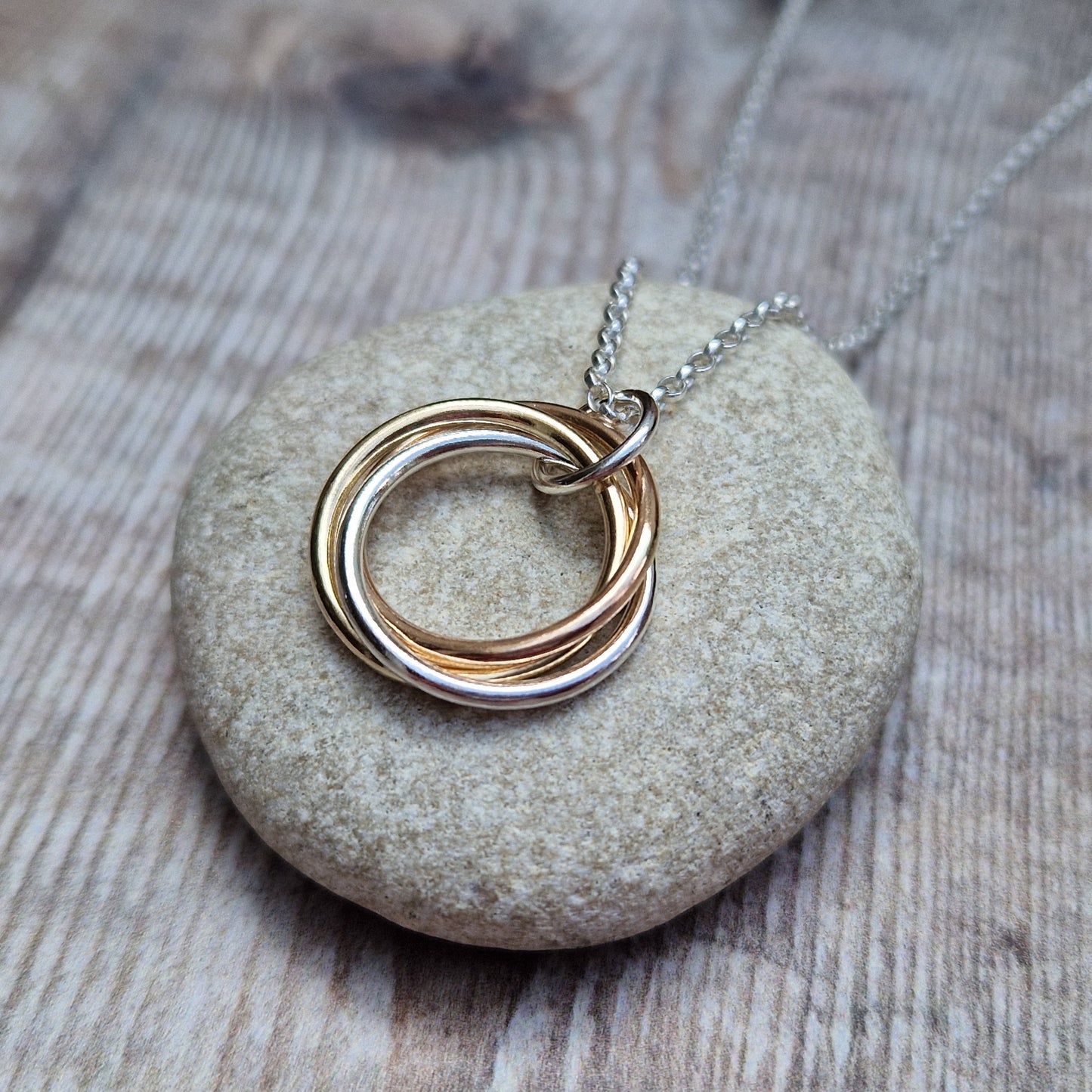 A detailed view of the Silver and Gold Three Linked Circle Necklace with intertwined gold and silver rings, resting on a smooth stone surface.