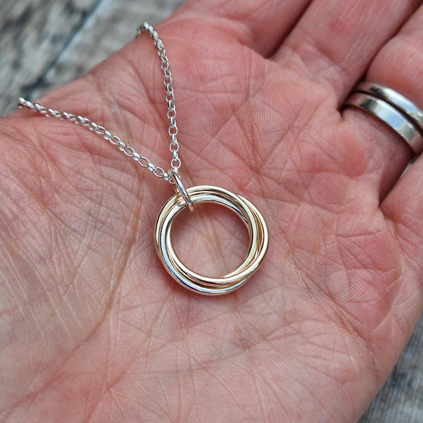 A hand holding a Silver and Gold Three Linked Circle Necklace with intertwined gold and silver rings on a delicate silver chain, highlighting the mix of metals.