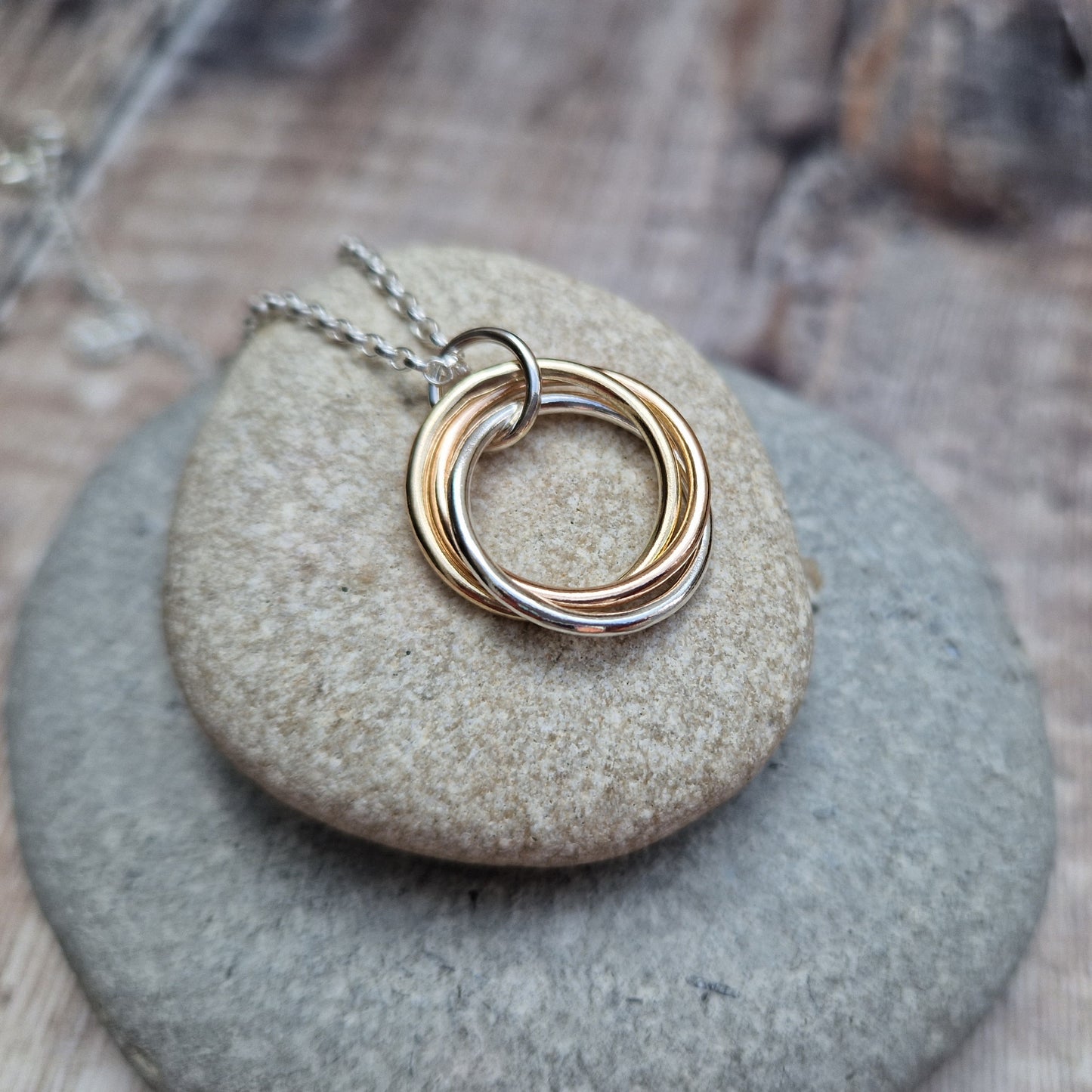 A detailed view of the Silver and Gold Three Linked Circle Necklace with intertwined gold and silver rings, resting on a smooth stone surface.