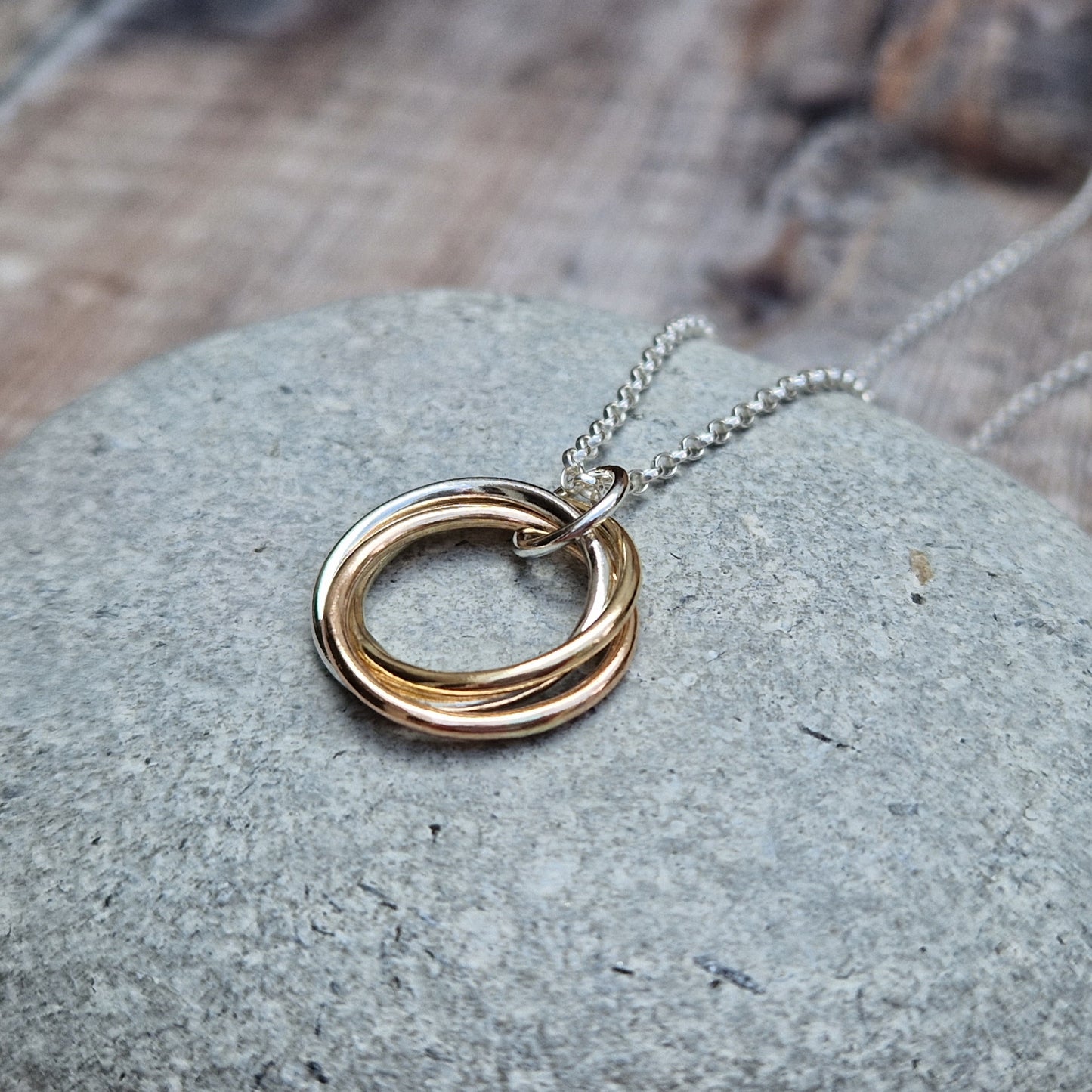 Silver and Gold Three Linked Circle Necklace. Three open circles, approximately 22mm in diameter, linked together as a Russian Ring (rings entwined). One circle is Sterling Silver, one is 9ct yellow gold and one is 9ct red gold. The pendant hangs from a silver necklace via a silver link.