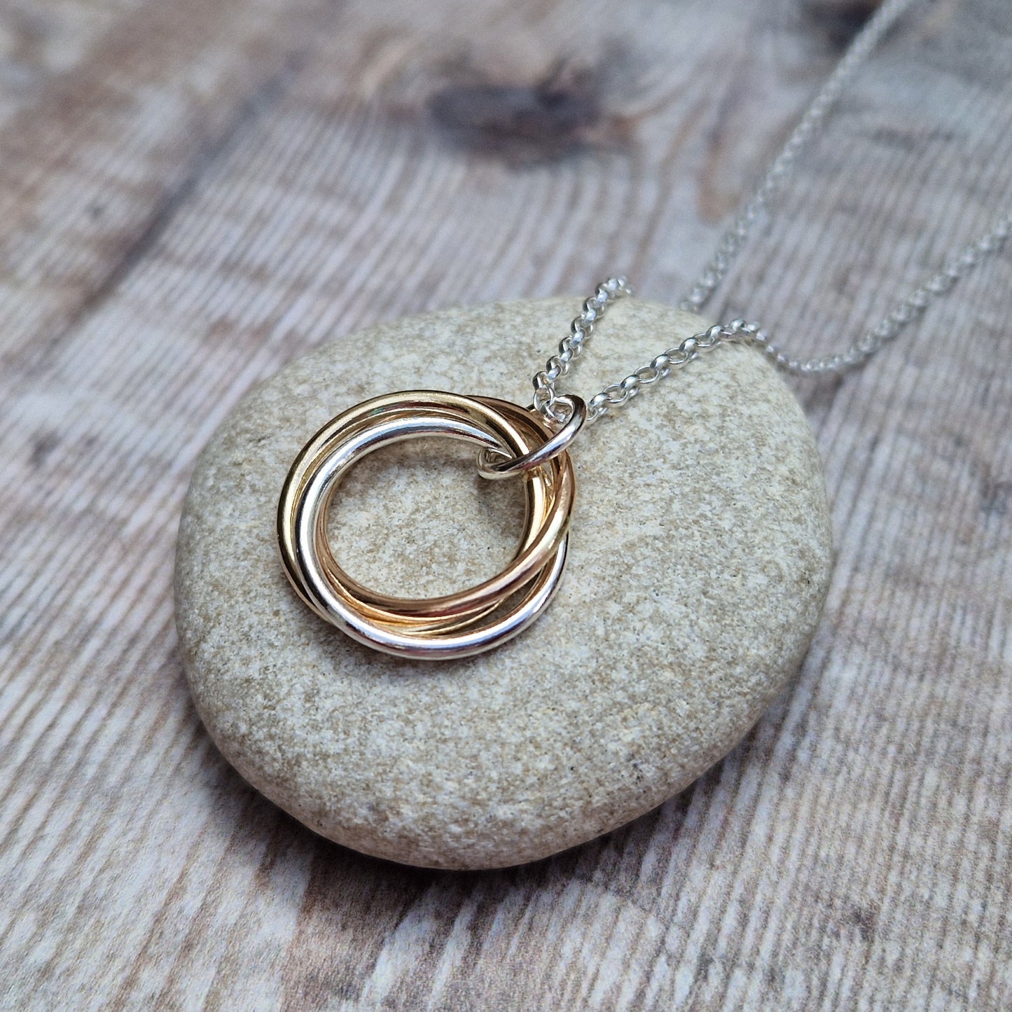 Silver and Gold Three Linked Circle Necklace Three open circles, approximately 22mm in diameter, linked together as a Russian Ring (rings entwined). One circle is Sterling Silver, one is 9ct yellow gold and one is 9ct red gold. The pendant hangs from a silver necklace via a silver link.