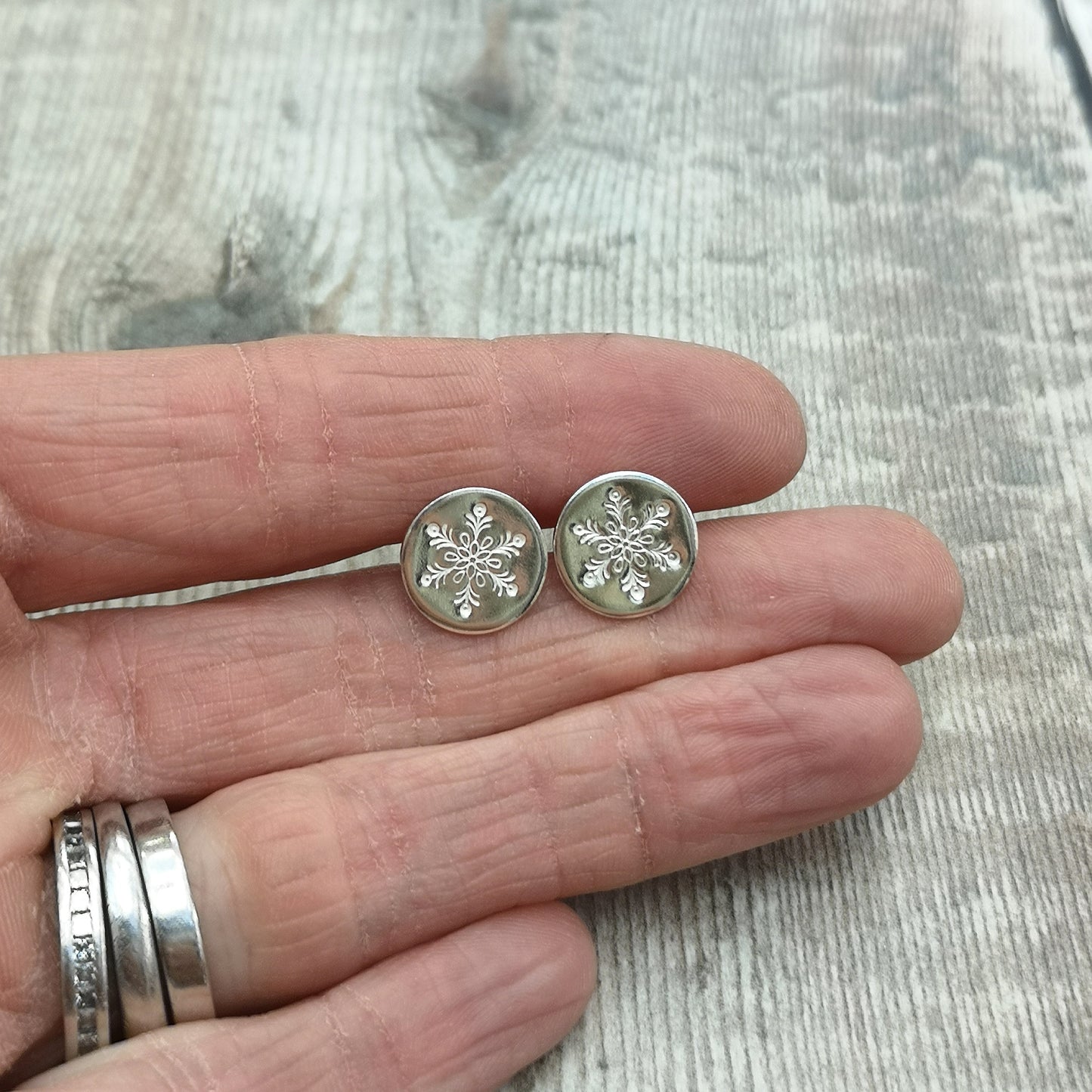 Each earring is a smooth silver disc shape stamped with one snowflake mounted onto a silver stud bar.