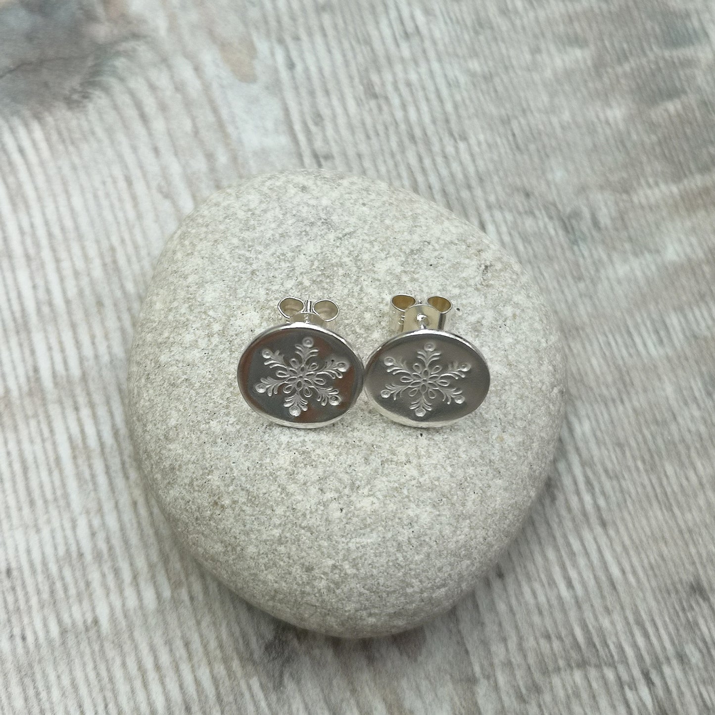 Each earring is a smooth silver disc shape stamped with one snowflake mounted onto a silver stud bar.