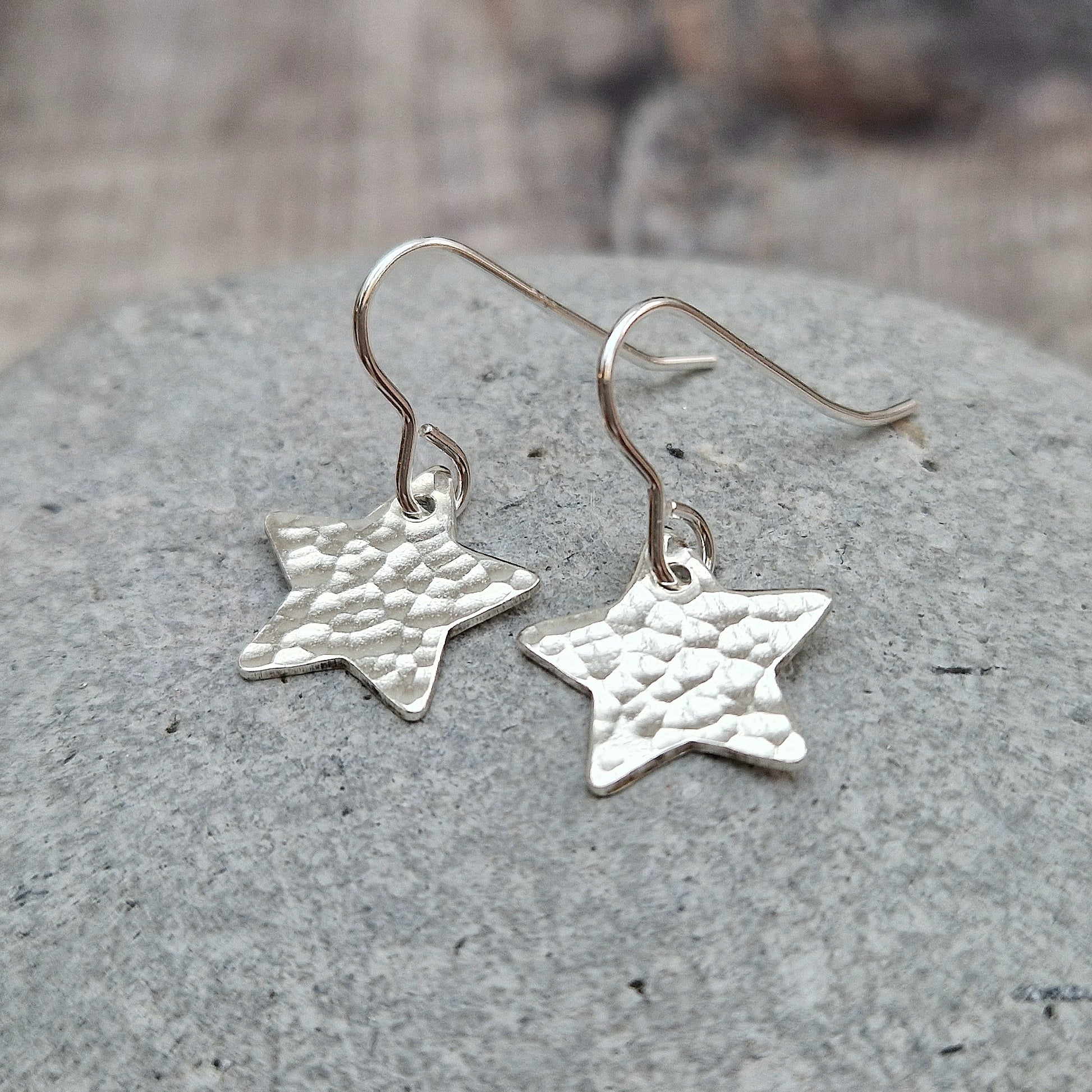 Each earring is a silver star shape with hammered texture finish suspended from silver earring wire.