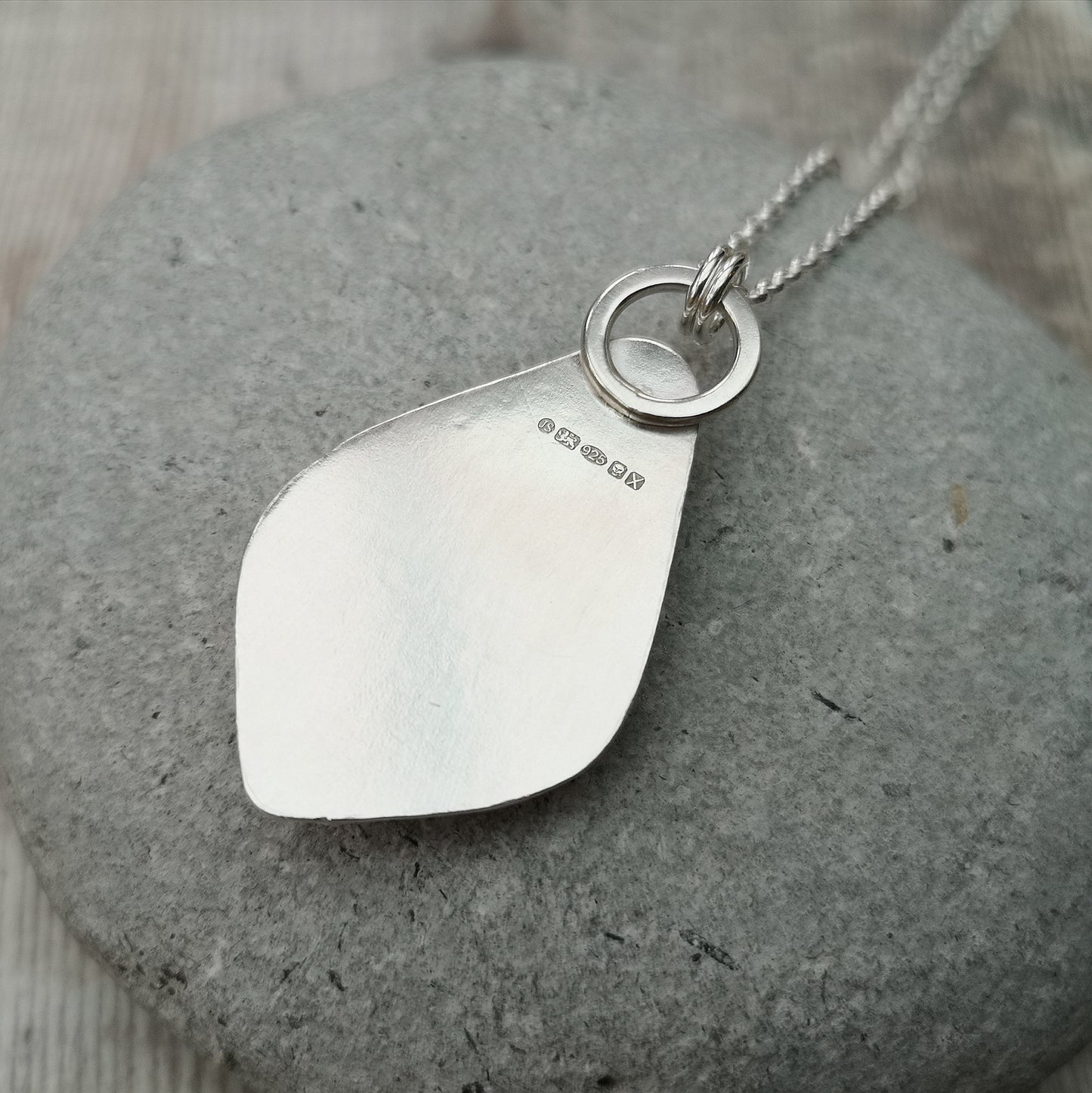 Pendant is a pear cut turquoise gemstone set in Sterling Silver bezel with small three silver sphere shapes set at the bottom of the bezel. Suspended from a silver chain via D-Link. The turquoise stone is blue with large plumes of black and brown.