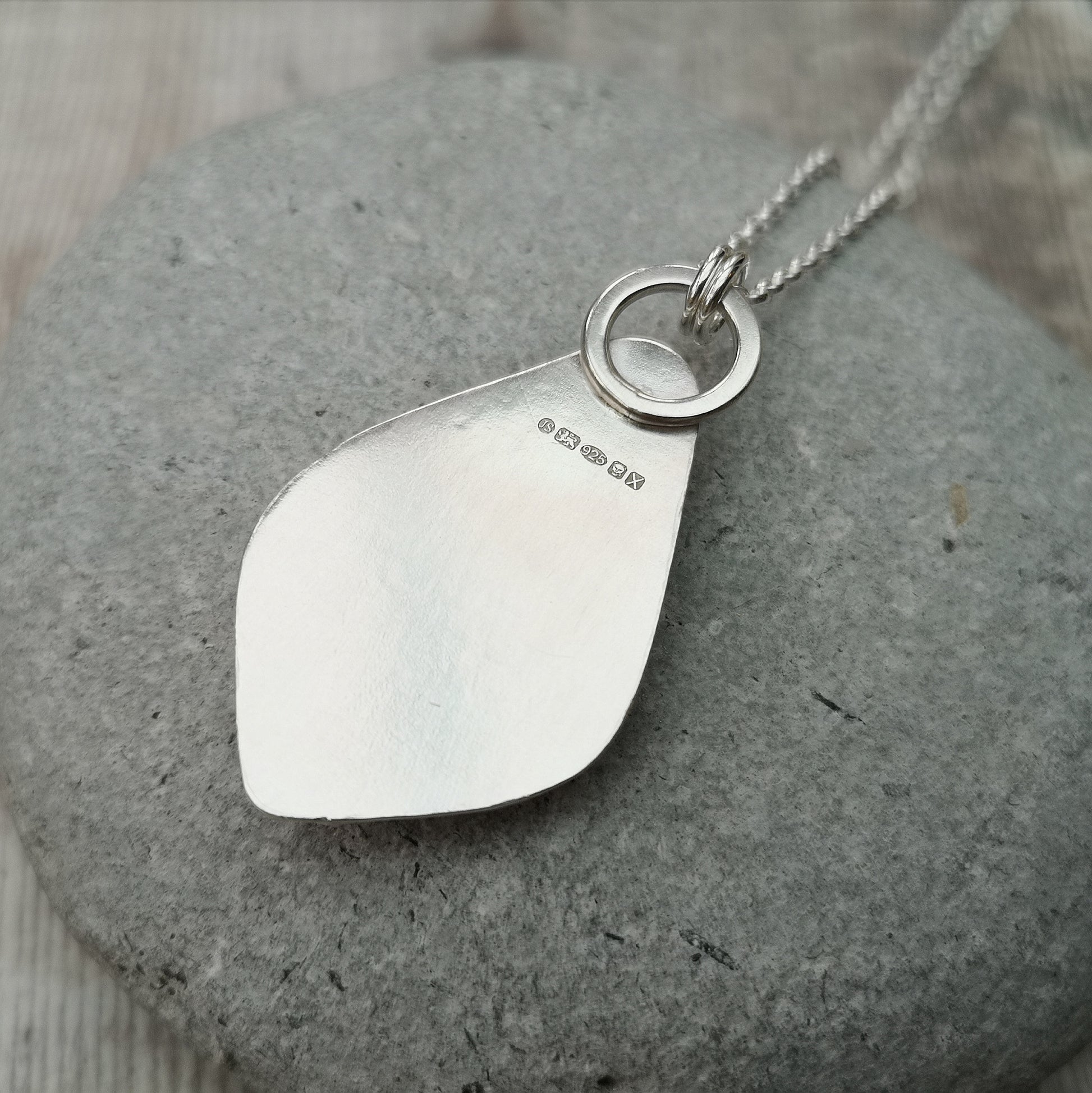 Pendant is a pear cut turquoise gemstone set in Sterling Silver bezel with small three silver sphere shapes set at the bottom of the bezel. Suspended from a silver chain via D-Link. The turquoise stone is blue with large plumes of black and brown.