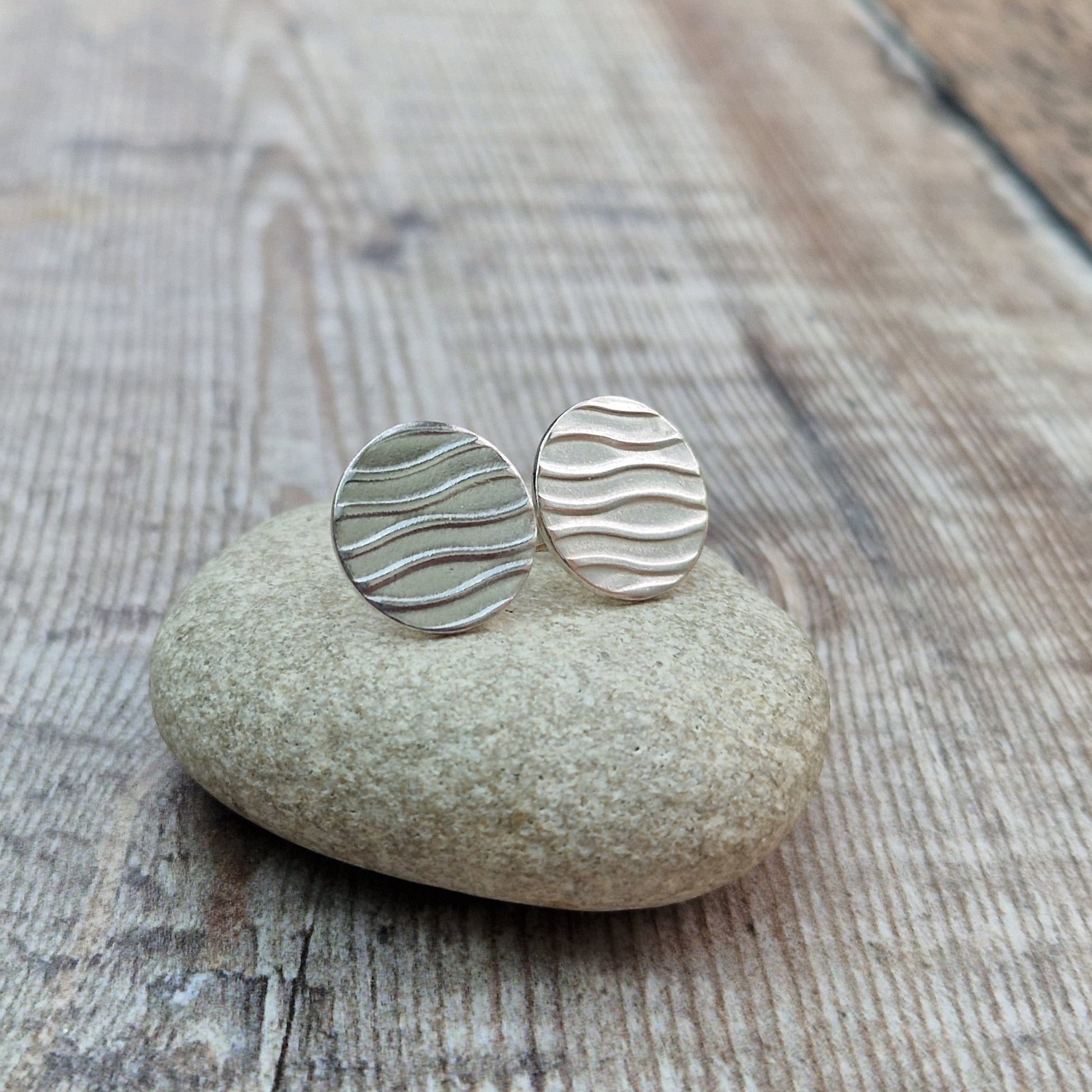 Each earring is a sterling silver disc stamped with a wavy line pattern. The wavy lines are spaced apart and raised from the disc, mounted on a silver stud bar.