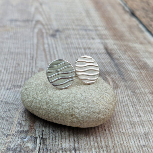 Each earring is a sterling silver disc stamped with a wavy line pattern. The wavy lines are spaced apart and raised from the disc, mounted on a silver stud bar.