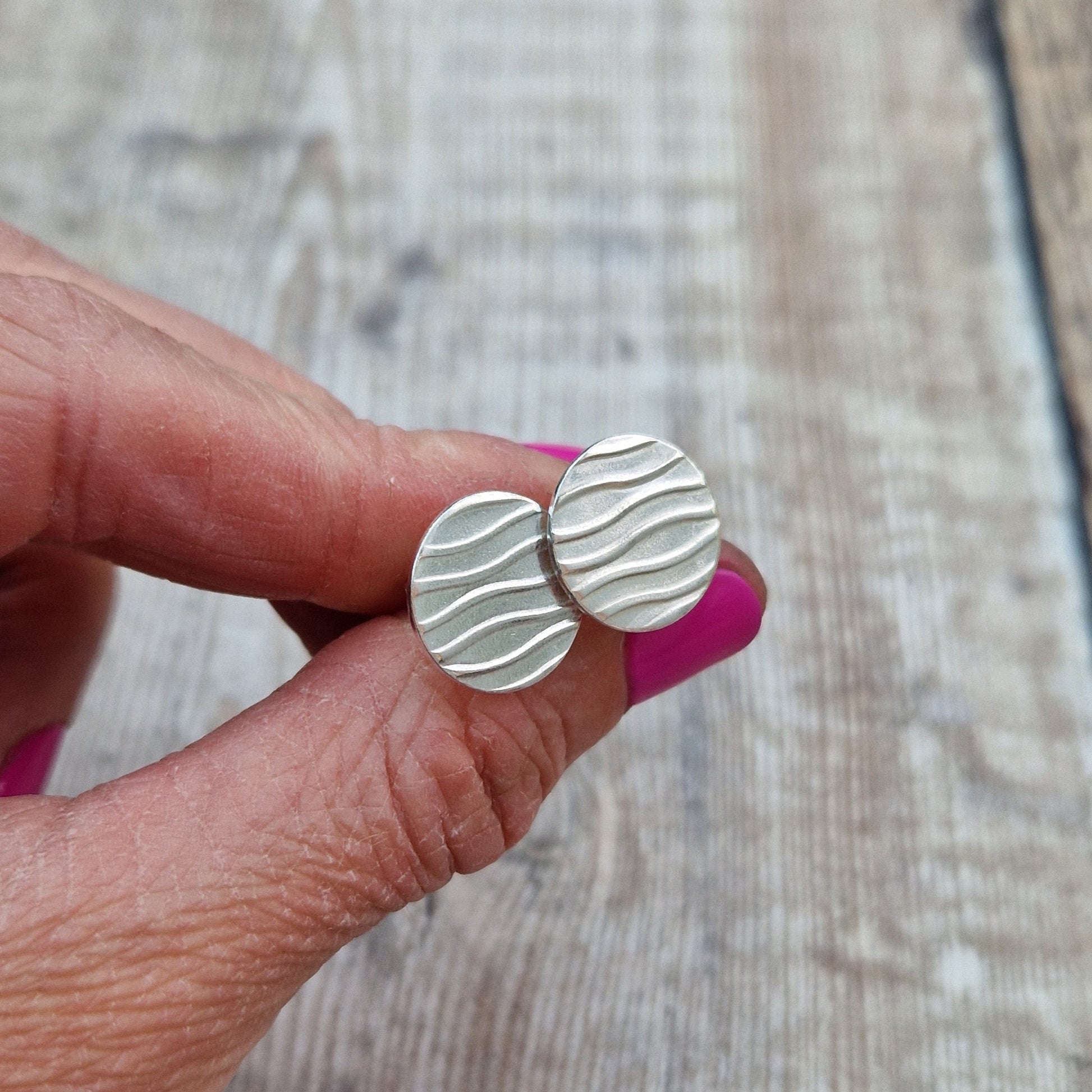 Each earring is a sterling silver disc stamped with a wavy line pattern. The wavy lines are spaced apart and raised from the disc, mounted on a silver stud bar.