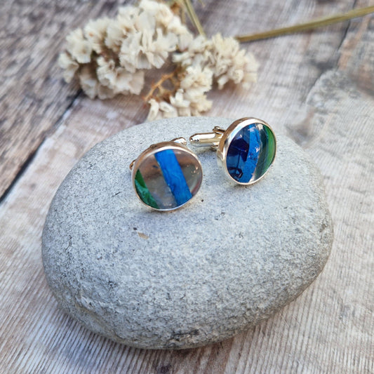 Silver Green and Blue Surfite cufflinks displayed on a grey stone. 