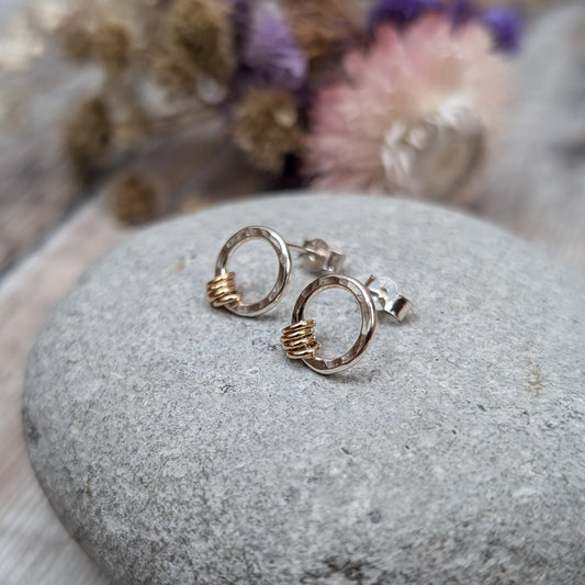 Silver Circle Stud Earrings with Gold Loops shown resting on a grey stone with dried flowers in the background.