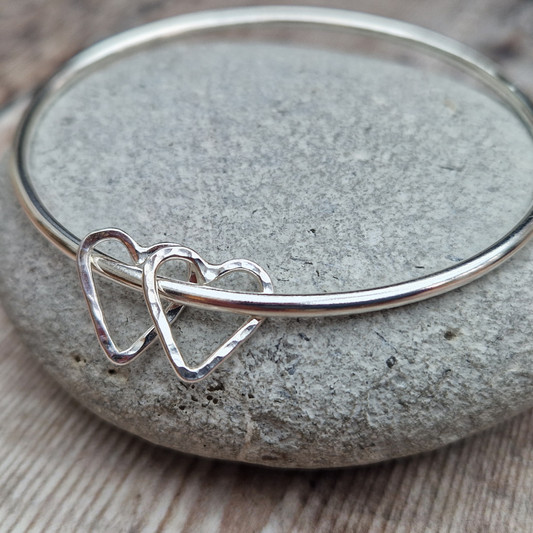 Silver Open Heart Bangle shown displayed on a grey stone. 