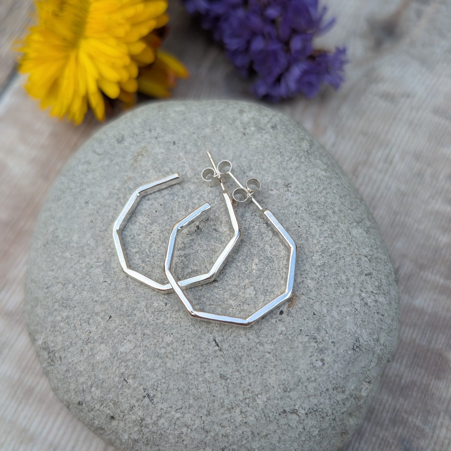 Silver hoops shown displayed on a grey stone with dried flowers in the background. 