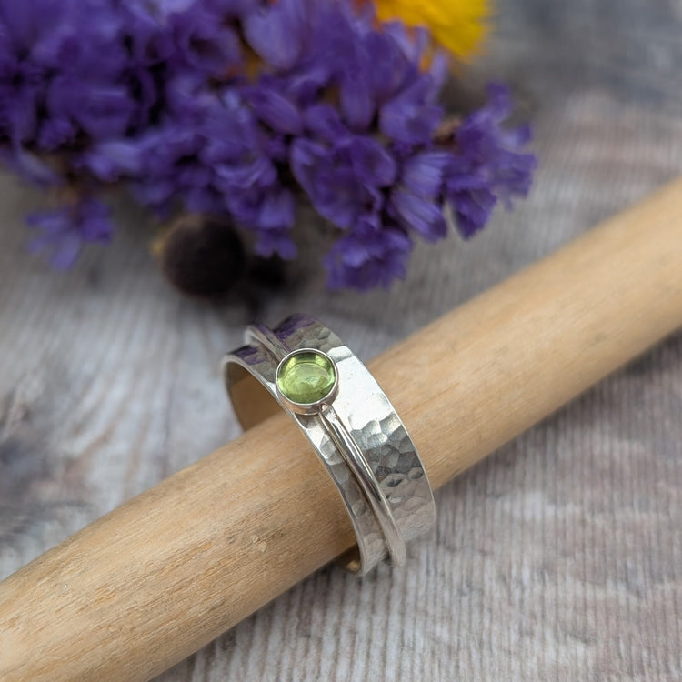 Ring shown displayed on a wooden dowl with dried flowers in the background.