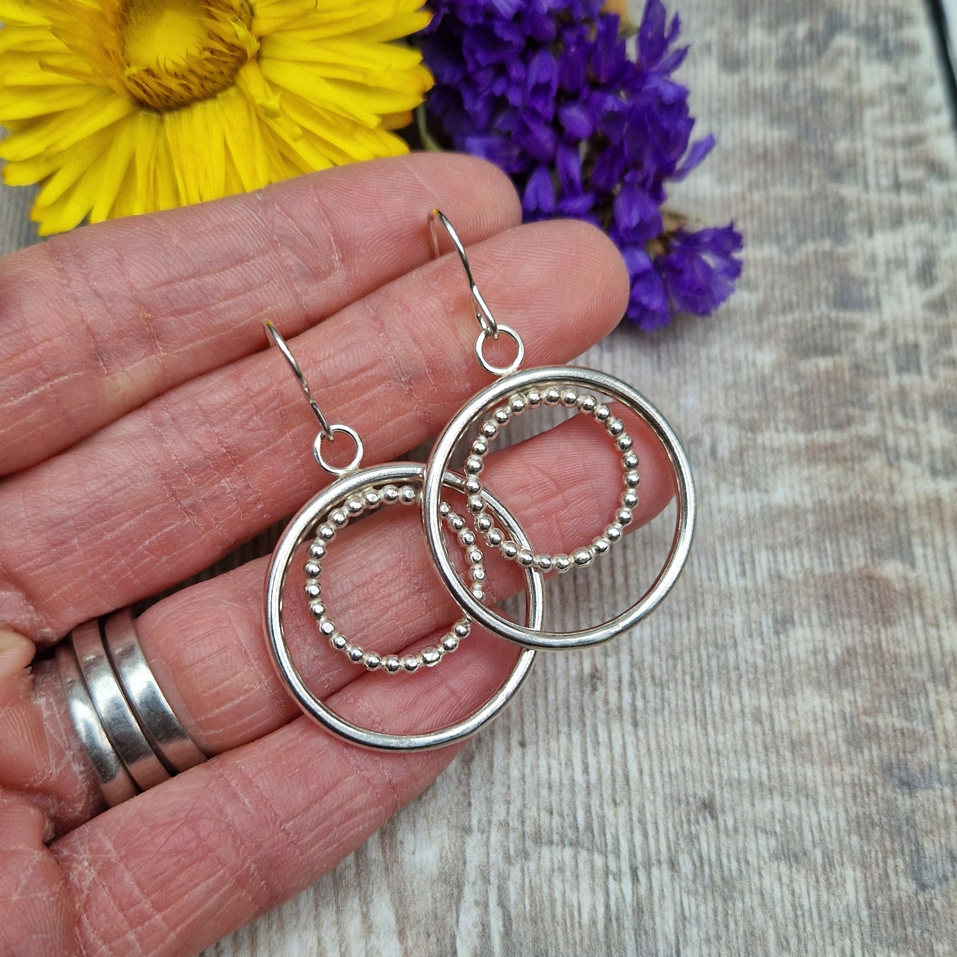 Each earring is one large silver open circle suspended from silver earring wire. A smaller beaded open circle is suspended from the top of the larger circle.