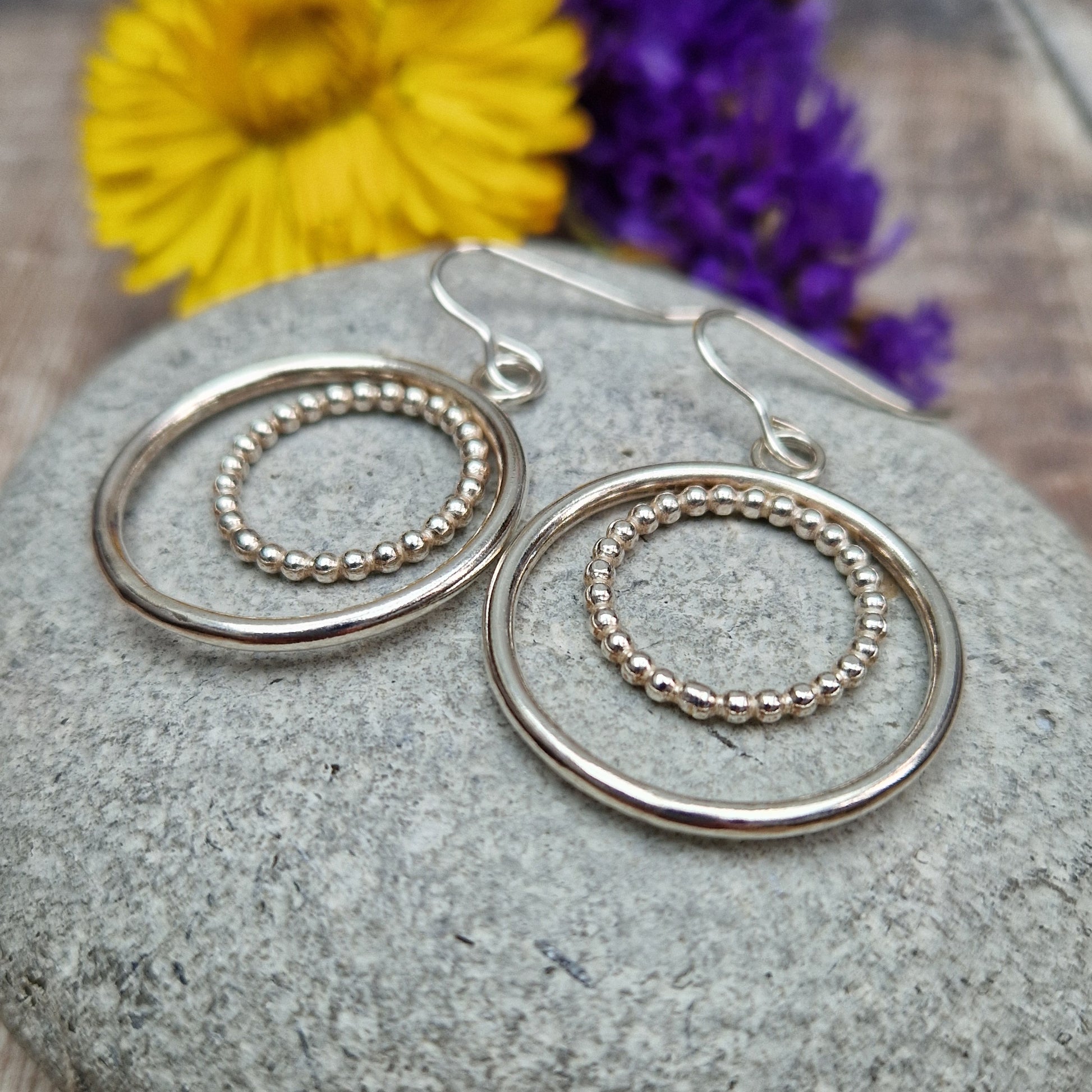 Each earring is one large silver open circle suspended from silver earring wire. A smaller beaded open circle is suspended from the top of the larger circle.