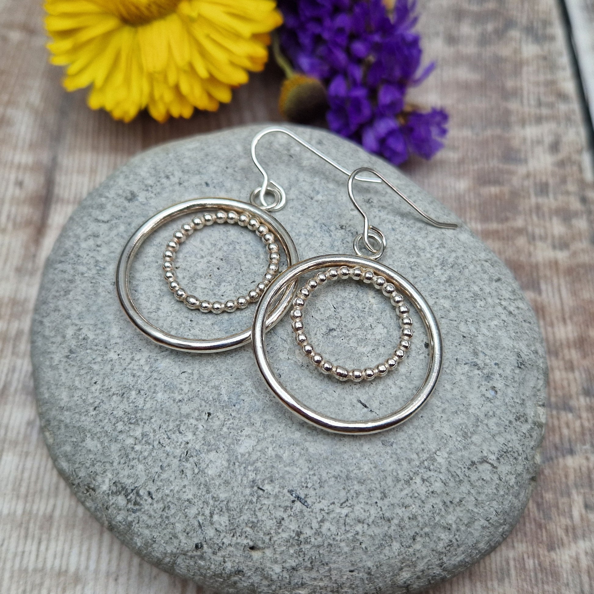 Each earring is one large silver open circle suspended from silver earring wire. A smaller beaded open circle is suspended from the top of the larger circle.