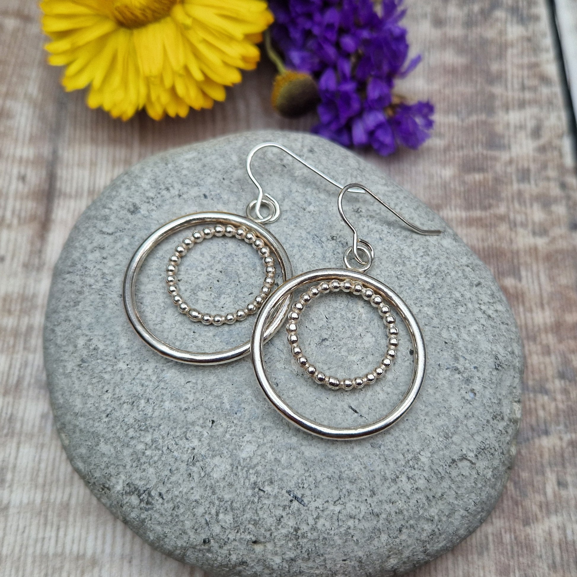 Each earring is one large silver open circle suspended from silver earring wire. A smaller beaded open circle is suspended from the top of the larger circle.