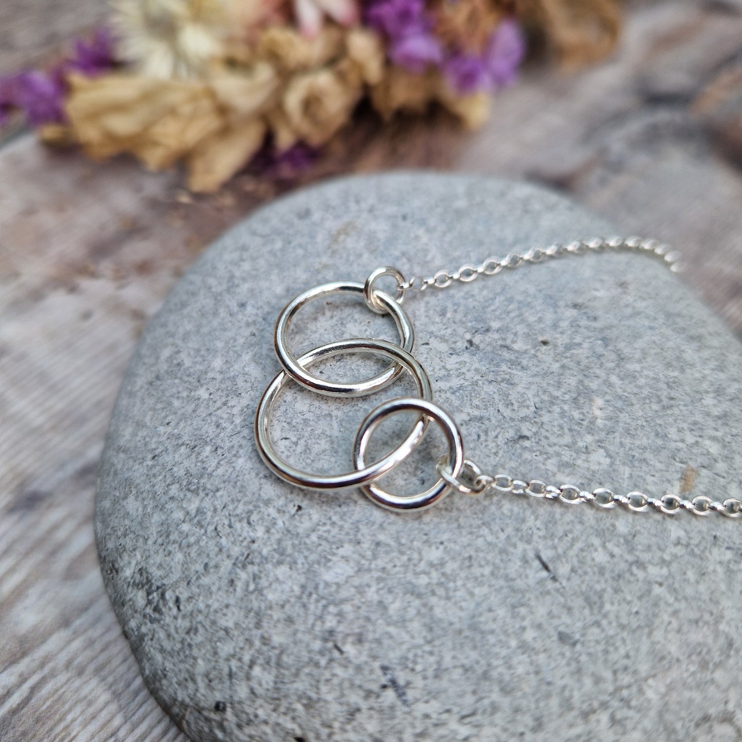 Three different sized Sterling Silver open circles linked together. Each outside circle is linked to a silver chain via small cirle links. The largest open circle is central.