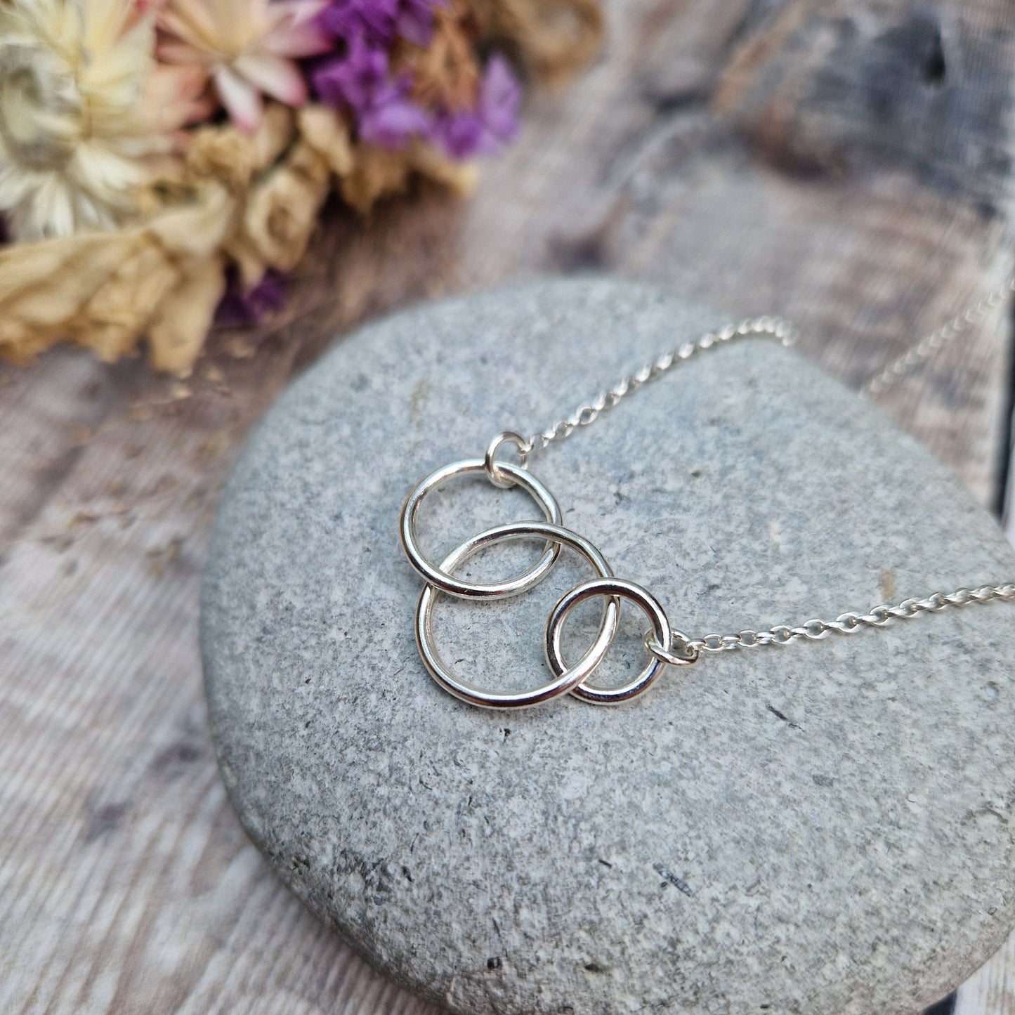 Three different sized Sterling Silver open circles linked together. Each outside circle is linked to a silver chain via small cirle links. The largest open circle is central.