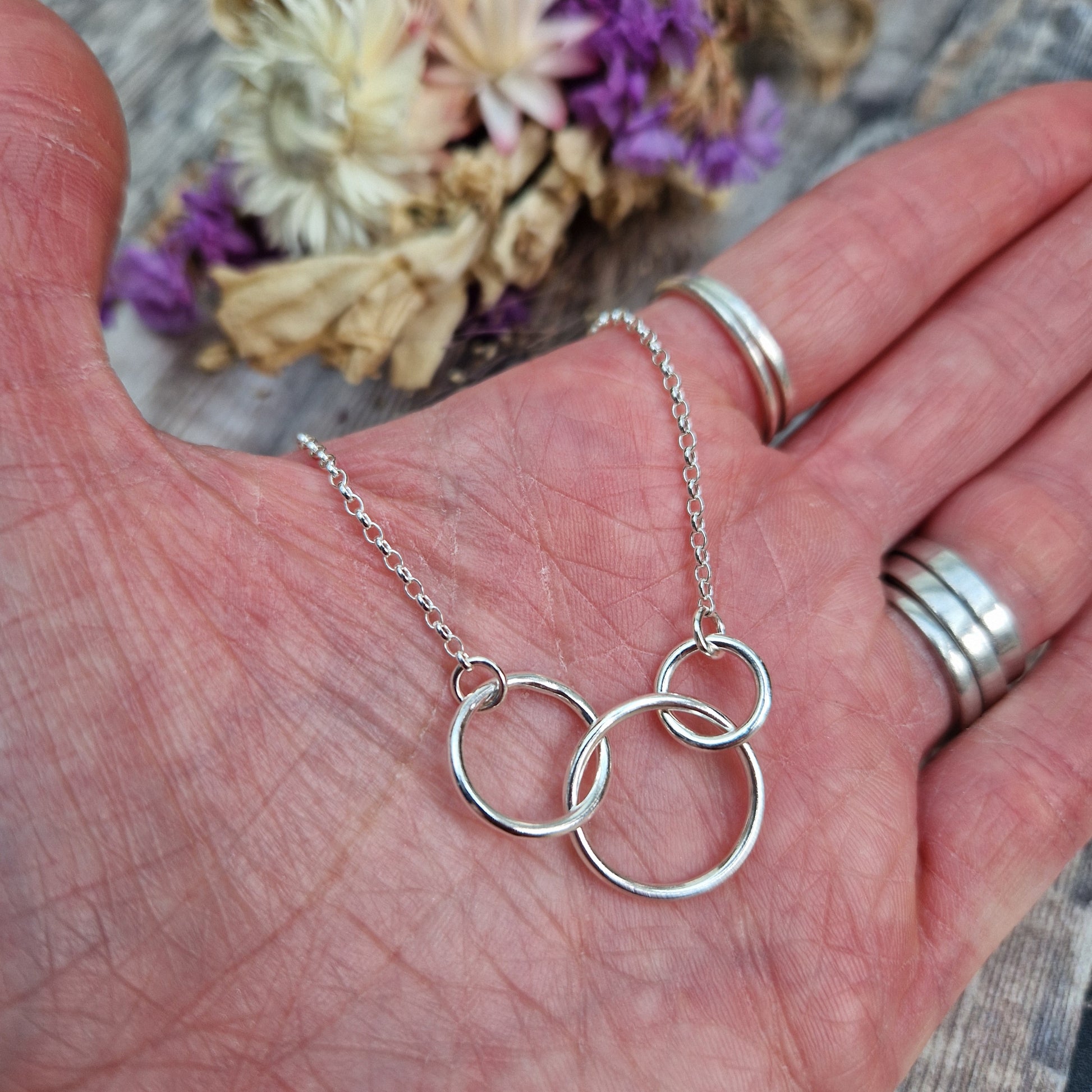 Three different sized Sterling Silver open circles linked together. Each outside circle is linked to a silver chain via small cirle links. The largest open circle is central.