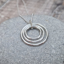 Load image into Gallery viewer, Sterling Silver three circle necklace. Three open silver concentric circles sat within each other, smallest in the centre. Attached to silver chain via small silver hoop. Largest circle measuring approximately 25mm diameter, smallest circle measuring approximately 15mm diameter. Chain length 16, 18 or 20 inches.