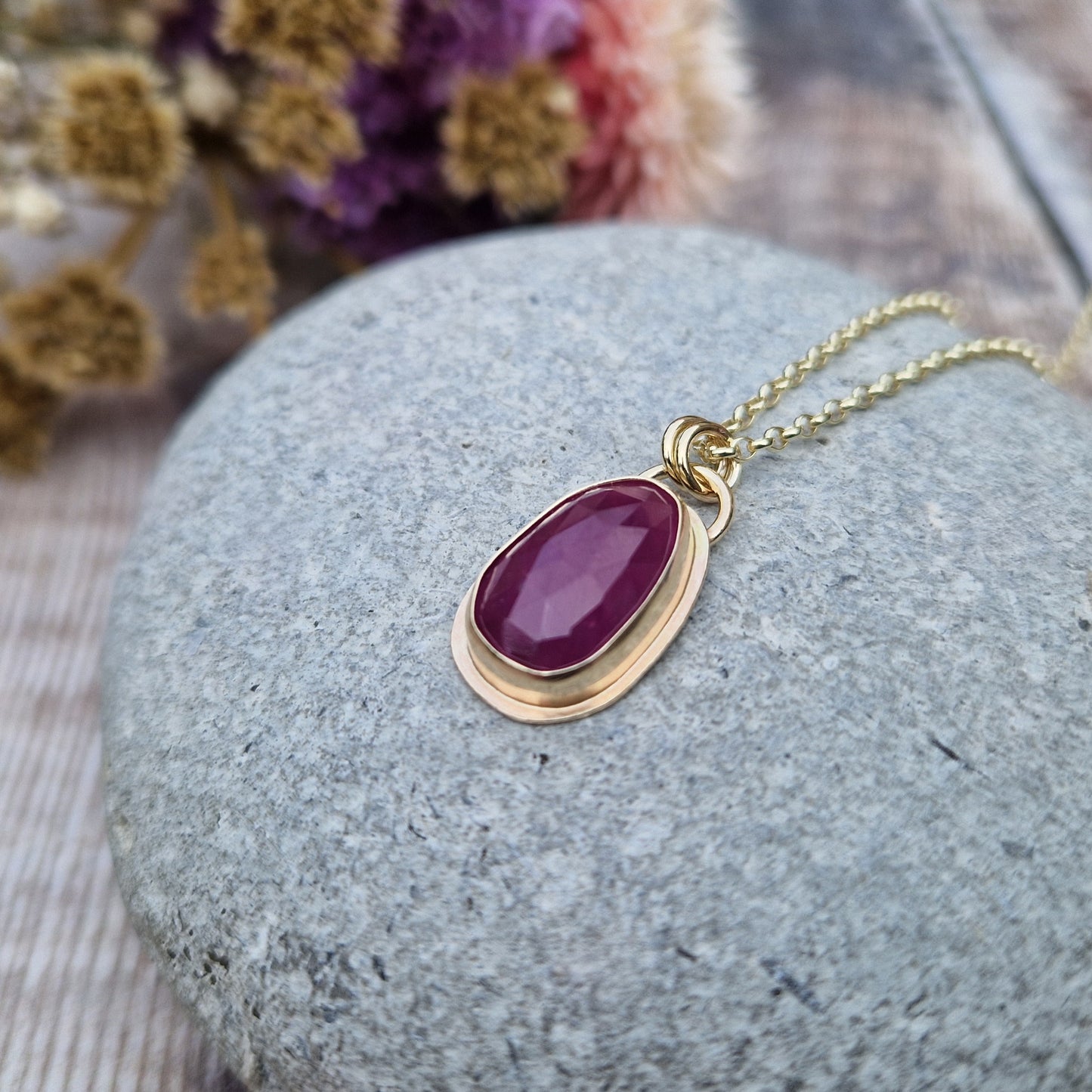 Statement 9ct gold necklace. Medium sized pendant approximately 12mm x 27mm is red sapphire, colour is dark mauve, slight texture to stone, like diamond cut. Set in gold surround. Gemstone is soft pear shaped, rounded at top. Attached to gold chain with two small circular gold links.