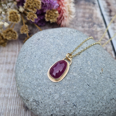Statement 9ct gold necklace. Medium sized pendant approximately 12mm x 27mm is red sapphire, colour is dark mauve, slight texture to stone, like diamond cut. Set in gold surround. Gemstone is soft pear shaped, rounded at top. Attached to gold chain with two small circular gold links.