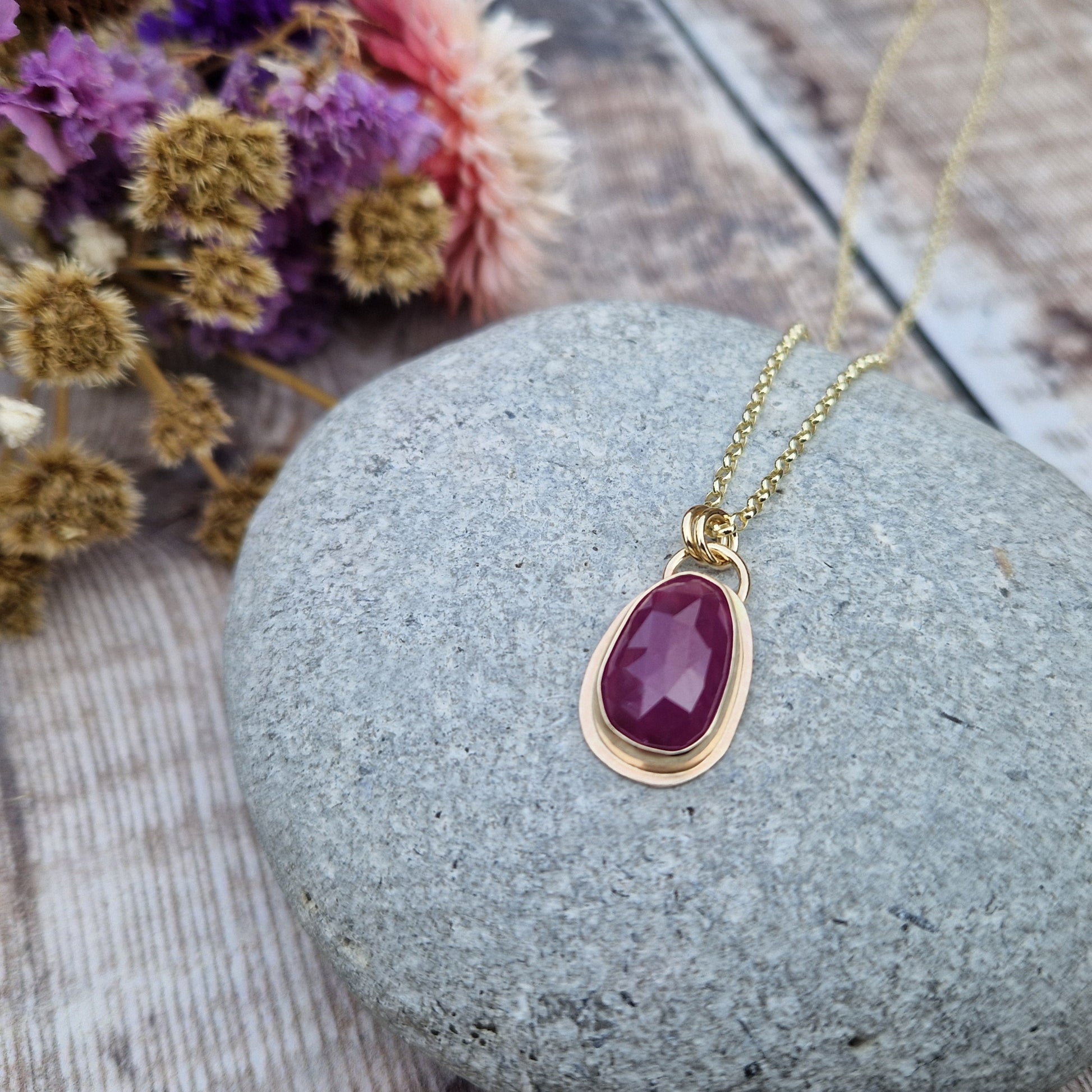 Statement 9ct gold necklace. Medium sized pendant approximately 12mm x 27mm is red sapphire, colour is dark mauve, slight texture to stone, like diamond cut. Set in gold surround. Gemstone is soft pear shaped, rounded at top. Attached to gold chain with two small circular gold links.