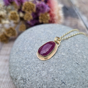 Statement 9ct gold necklace. Medium sized pendant approximately 12mm x 27mm is red sapphire, colour is dark mauve, slight texture to stone, like diamond cut. Set in gold surround. Gemstone is soft pear shaped, rounded at top. Attached to gold chain with two small circular gold links.