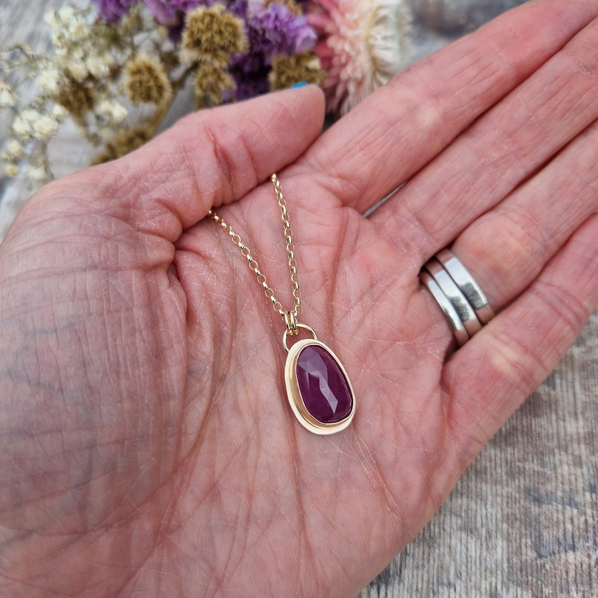 Statement 9ct gold necklace. Medium sized pendant approximately 12mm x 27mm is red sapphire, colour is dark mauve, slight texture to stone, like diamond cut. Set in gold surround. Gemstone is soft pear shaped, rounded at top. Attached to gold chain with two small circular gold links.