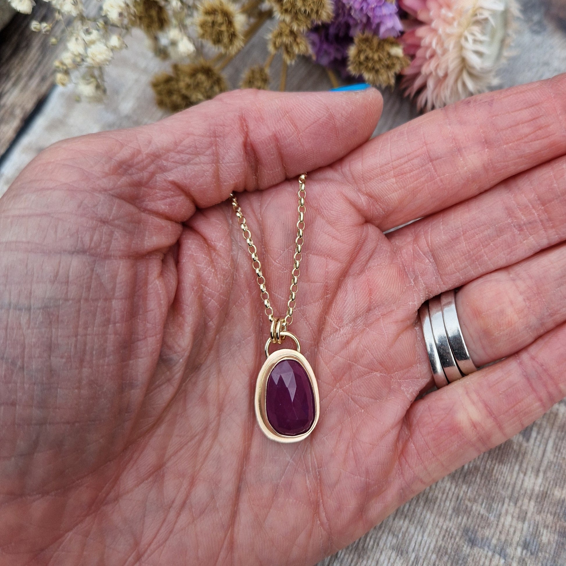 Statement 9ct gold necklace. Medium sized pendant approximately 12mm x 27mm is red sapphire, colour is dark mauve, slight texture to stone, like diamond cut. Set in gold surround. Gemstone is soft pear shaped, rounded at top. Attached to gold chain with two small circular gold links.