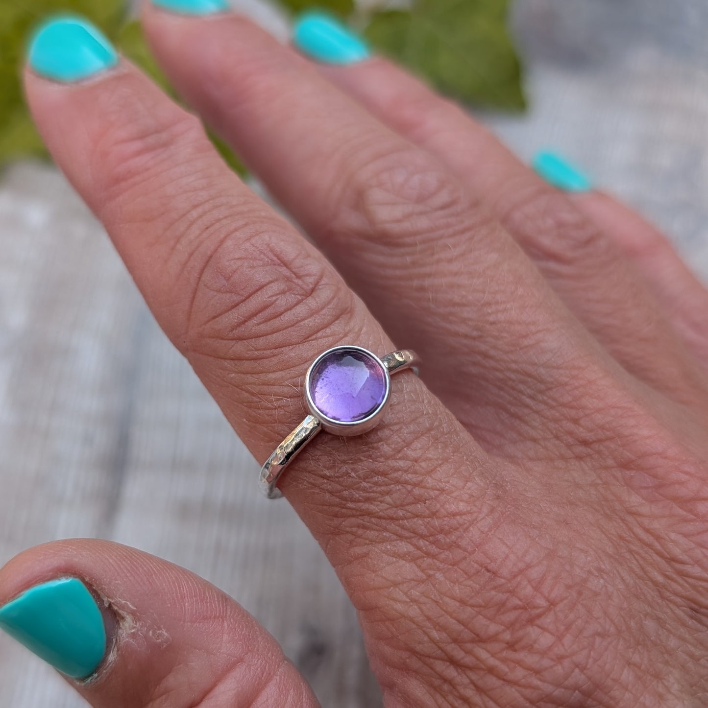 Amethyst ring size S handmade from recycled Sterling Silver, worn on a finger with the round purple Amethyst gemstone shown in natural light.