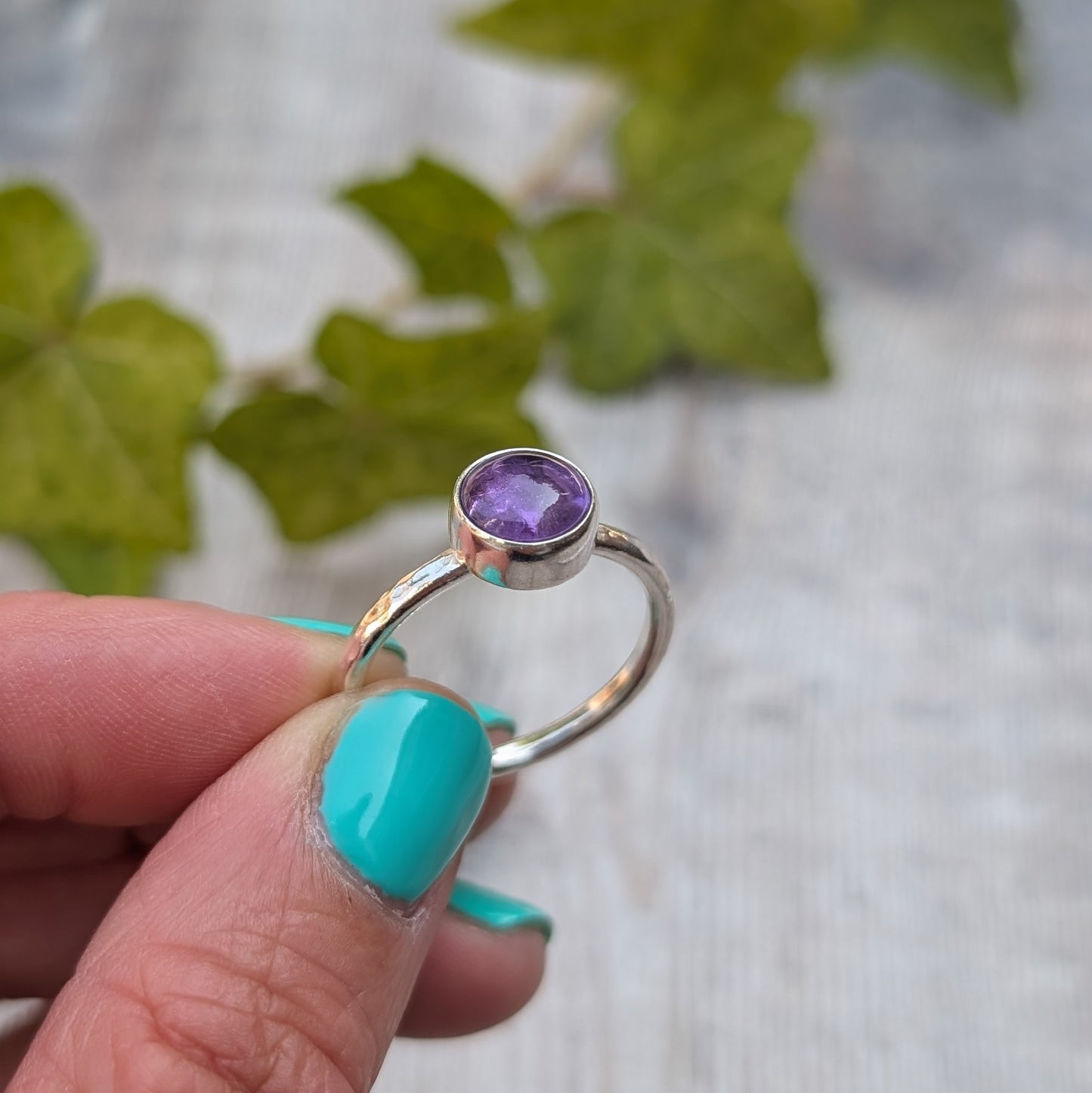 Amethyst ring size S handmade from recycled Sterling Silver, held between fingers showing the side profile of the round bezel set Amethyst gemstone.